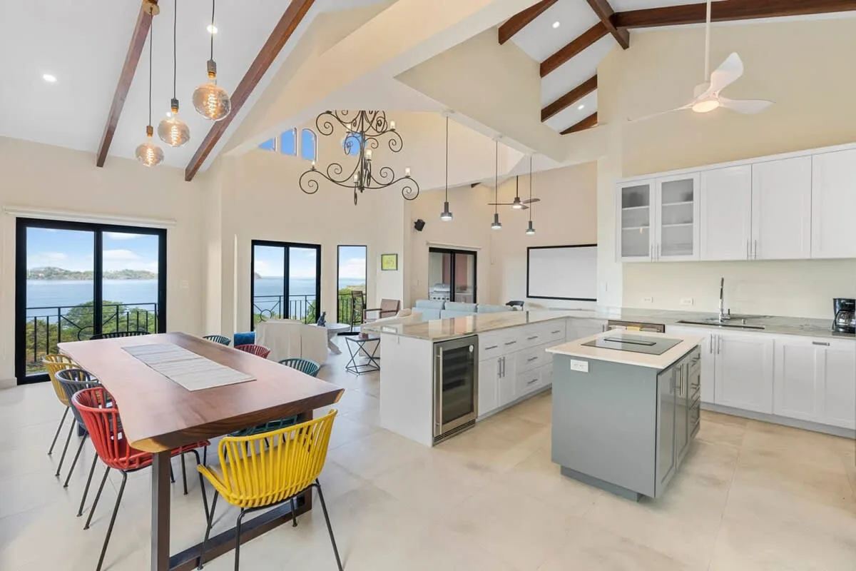 A bright open kitchen and dining area with a large table and windows overlooking the water.