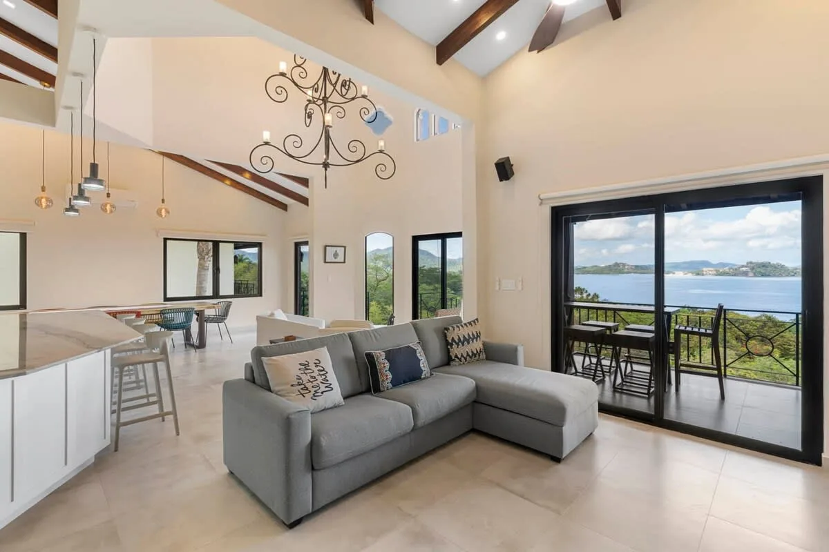 An open-plan living area with gray seating and wide glass doors overlooking the water.