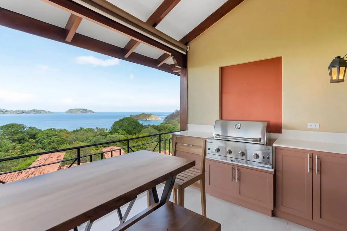 A covered outdoor kitchen and dining area overlooks green hills and the water.