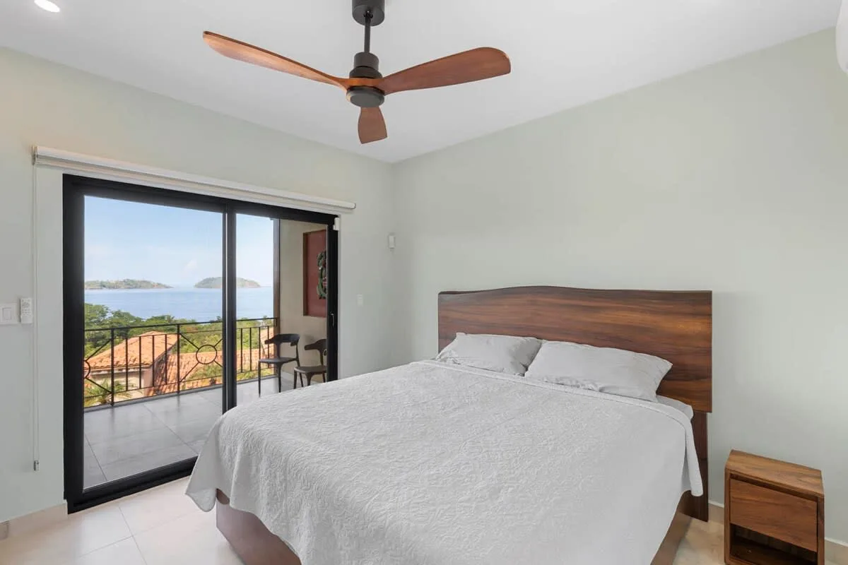 A bedroom with a large bed beside sliding glass doors opening to a balcony.