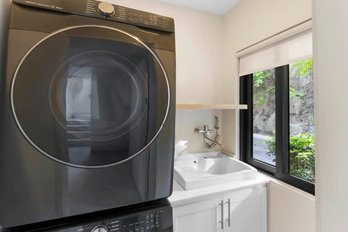 A laundry area with a front-loading washer beside a sink and window.