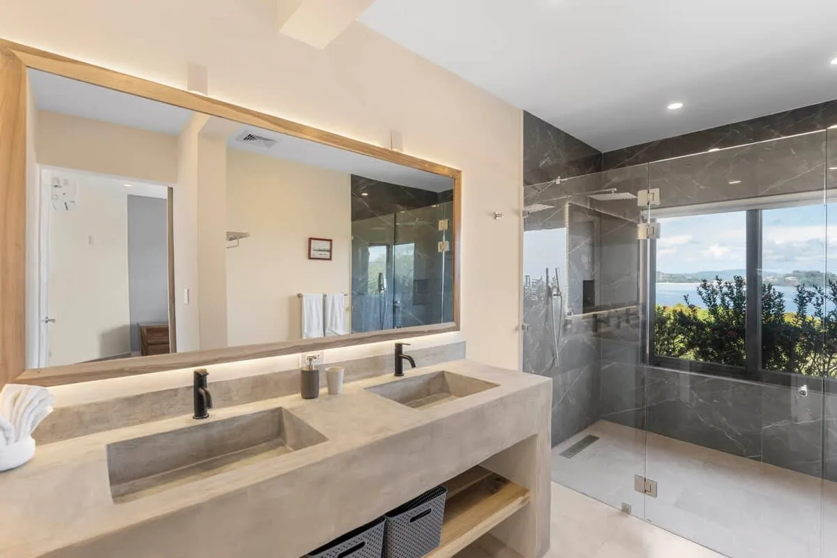 A bathroom vanity with a wide mirror beside a glass shower.