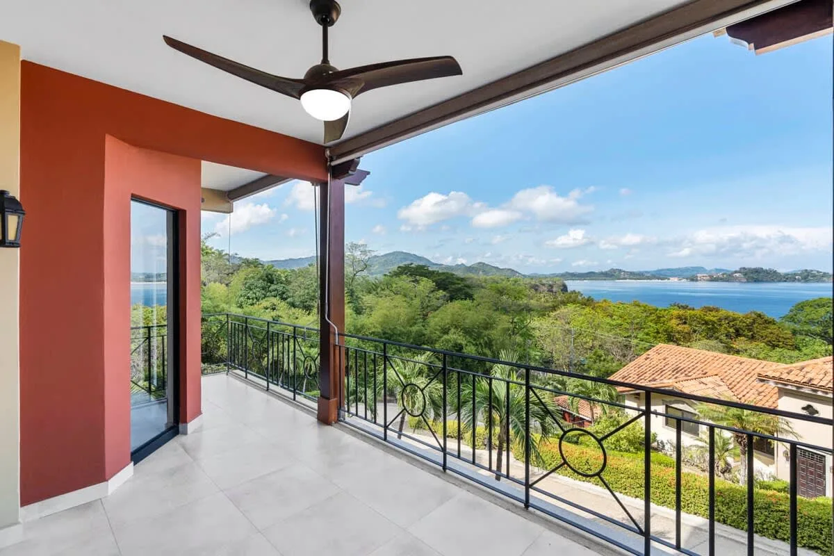 A covered balcony overlooks green hills and a coastal bay.