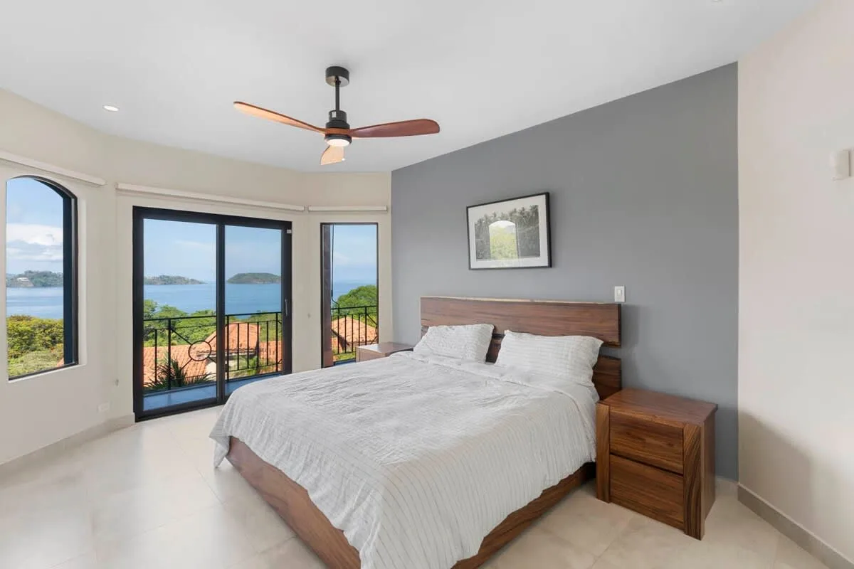 A bedroom with a bed beside wide windows overlooking the water.