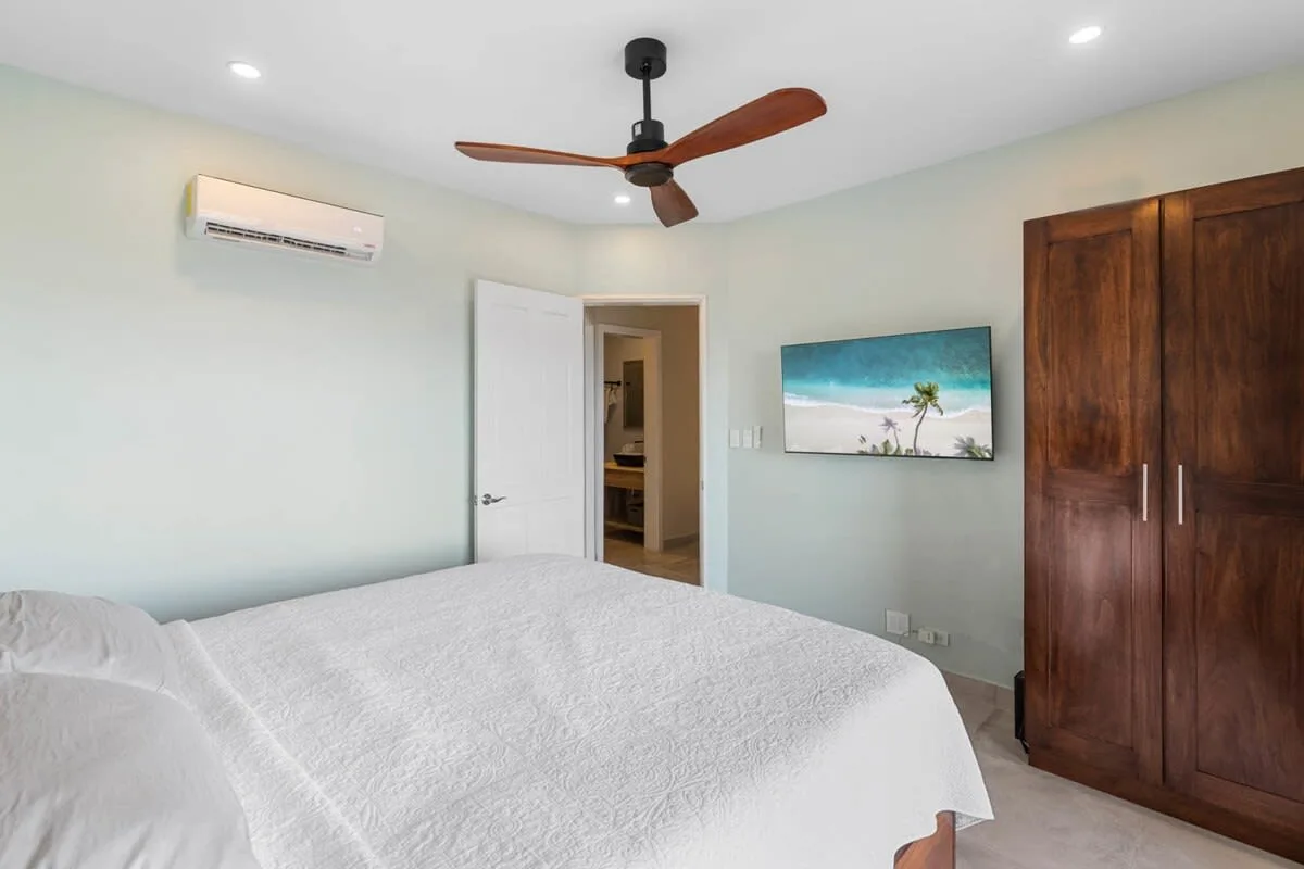 A bedroom with a bed, a wooden wardrobe, and a ceiling fan.