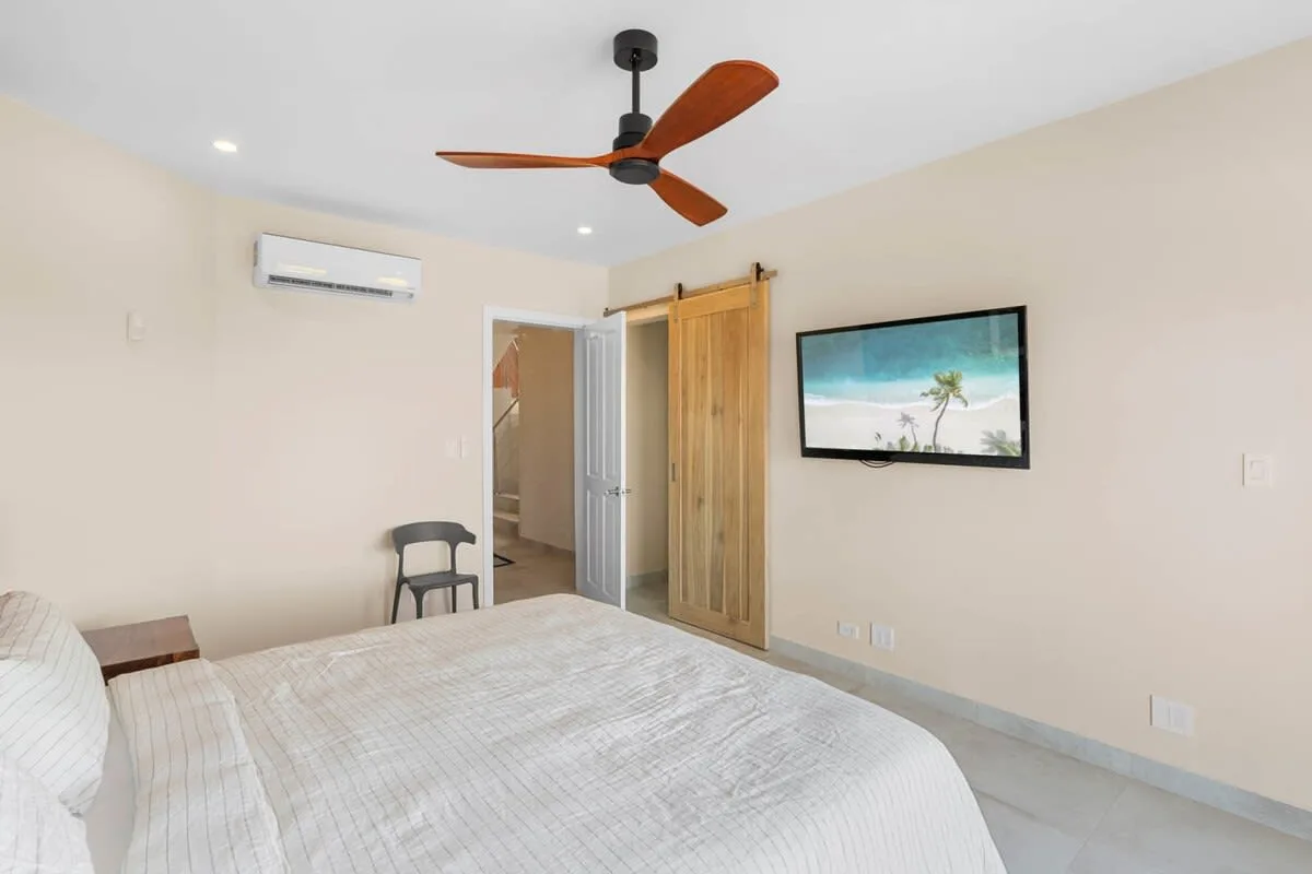 A bedroom with a bed, wooden door, and wall-mounted television.