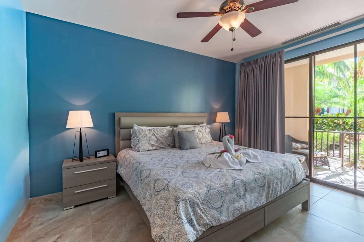 Un dormitorio con una cama grande, paredes azules y puertas de vidrio hacia un balcón.