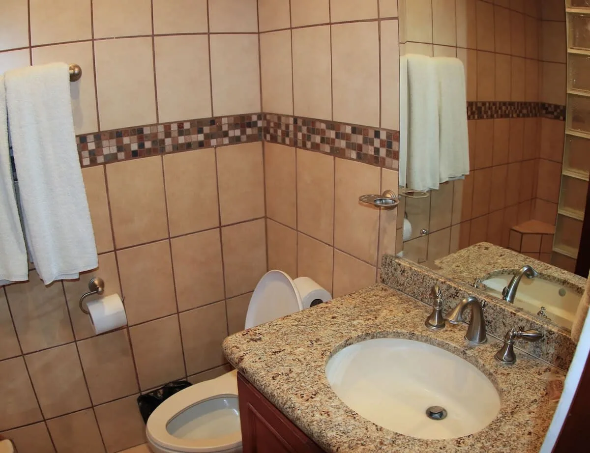 A tiled bathroom with a granite vanity, sink, and toilet.
