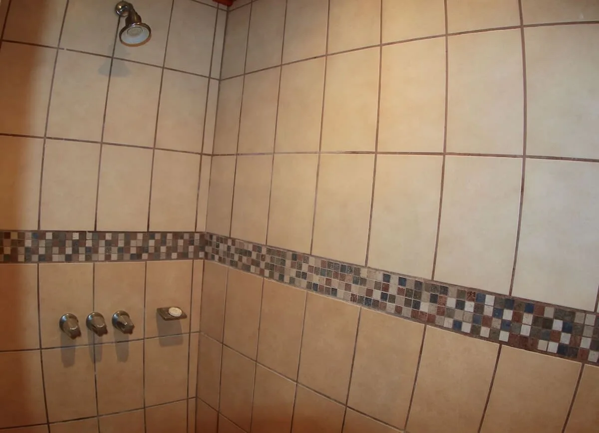 A tiled shower with wall-mounted controls and a decorative mosaic border.