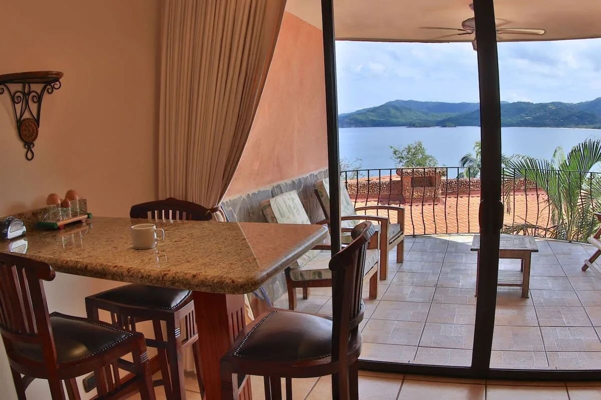 A dining area opens onto a covered terrace overlooking a lake and hills.