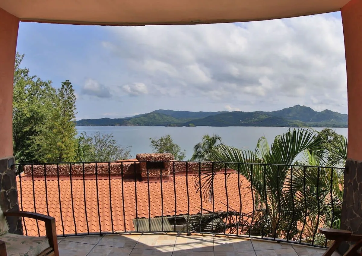 A covered terrace overlooks tiled rooftops, a lake, and green hills.