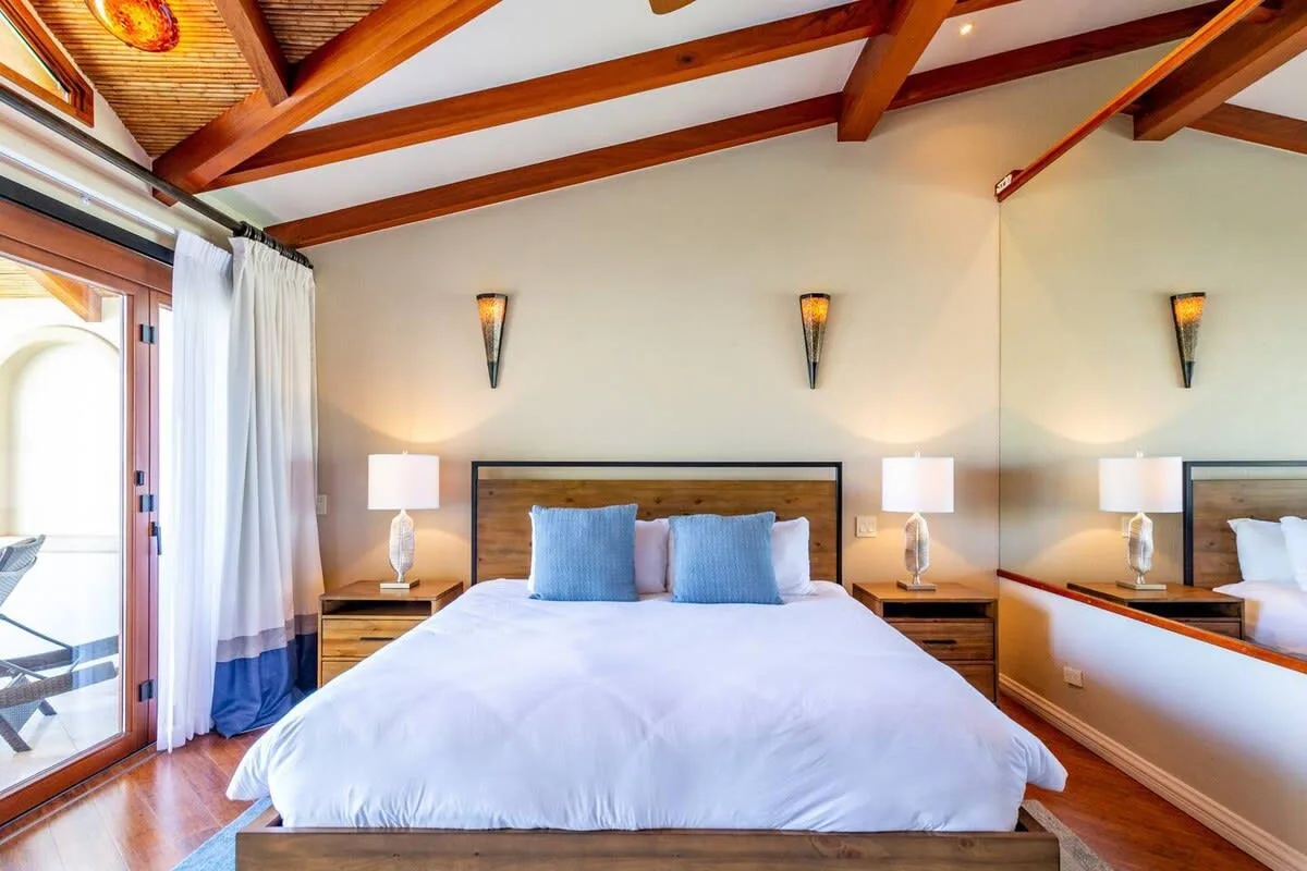 A bedroom with a large bed, bedside tables, and exposed wooden ceiling beams.
