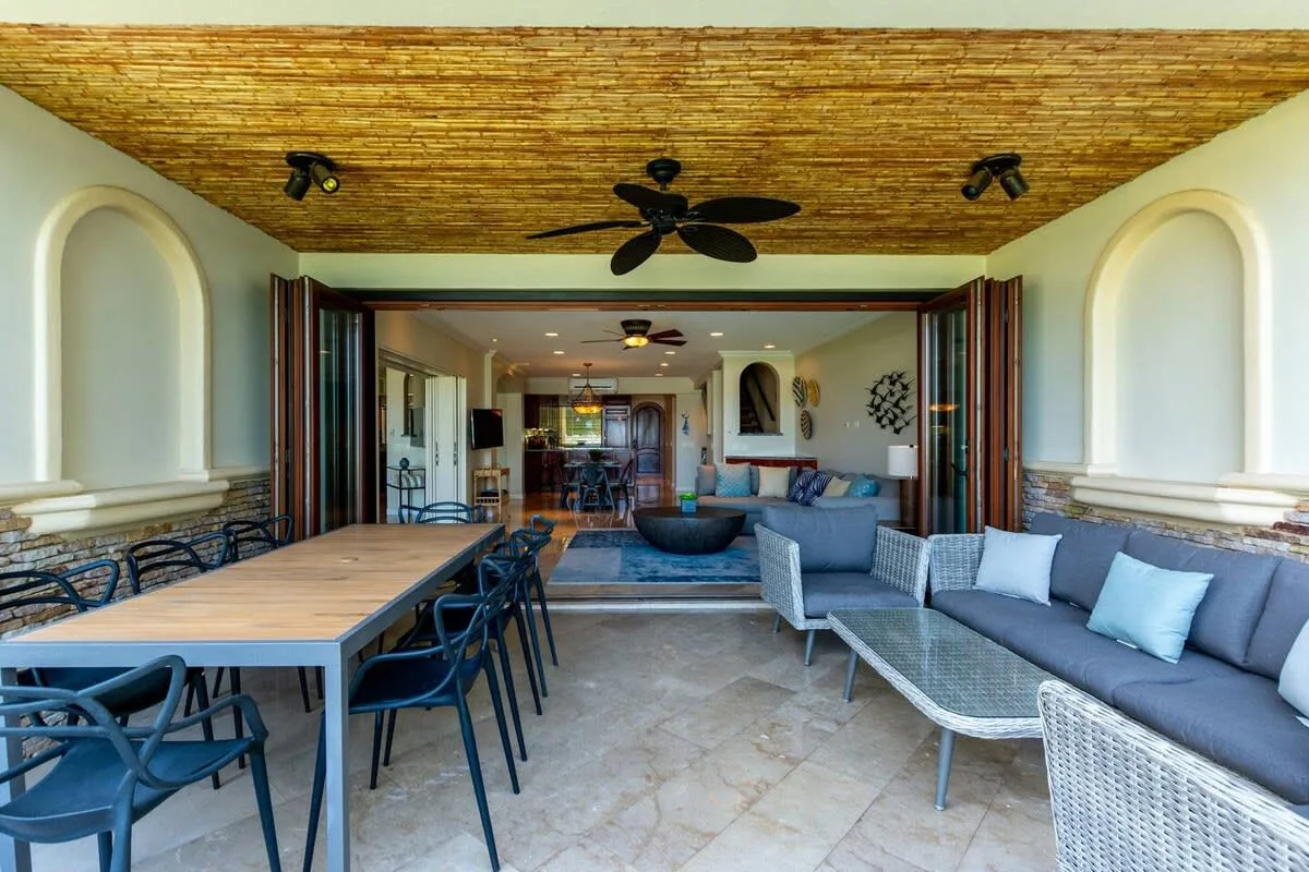 An open-air dining and lounge area with a long table and cushioned seating.
