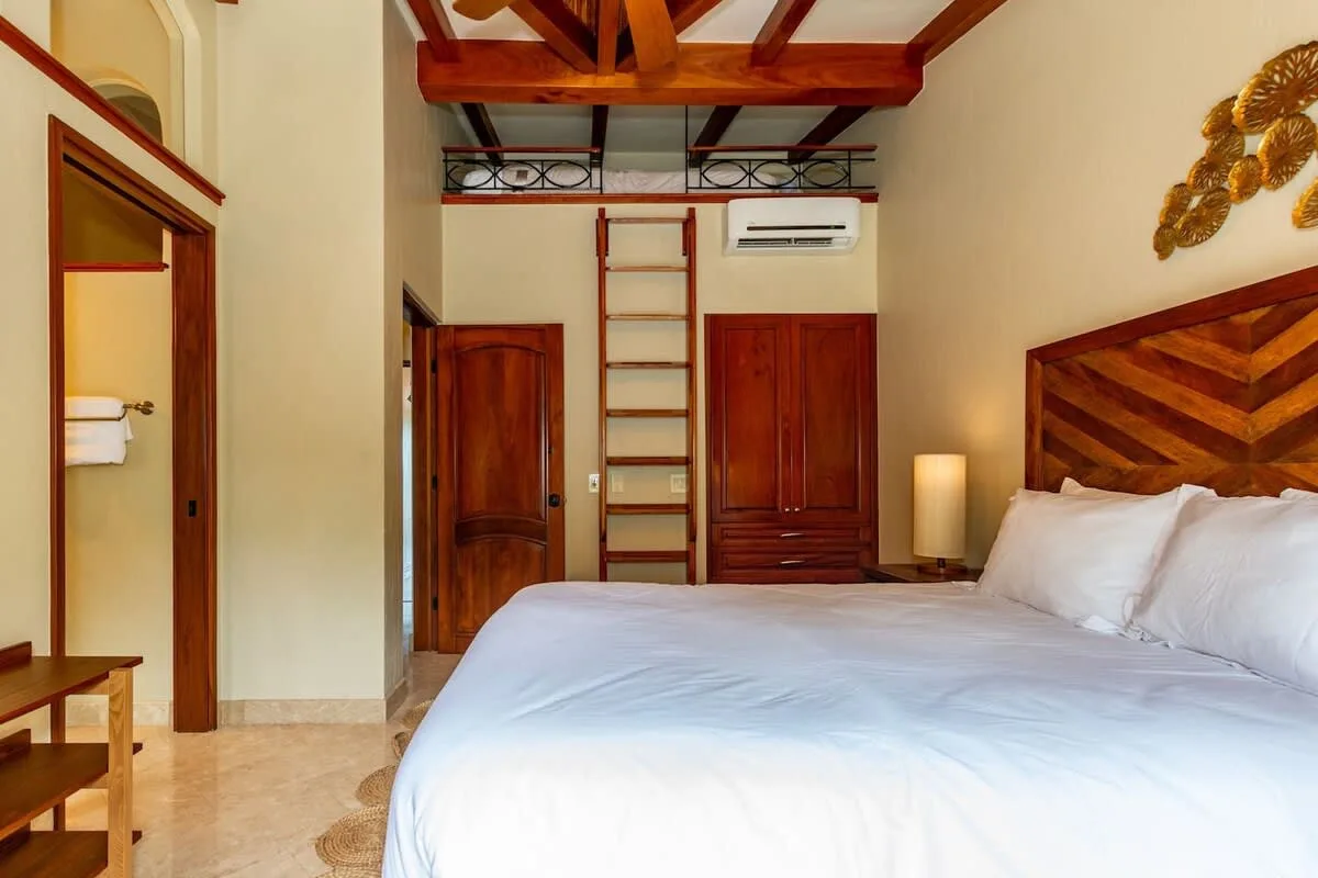 A bedroom with a large bed, wooden headboard, and exposed ceiling beams.