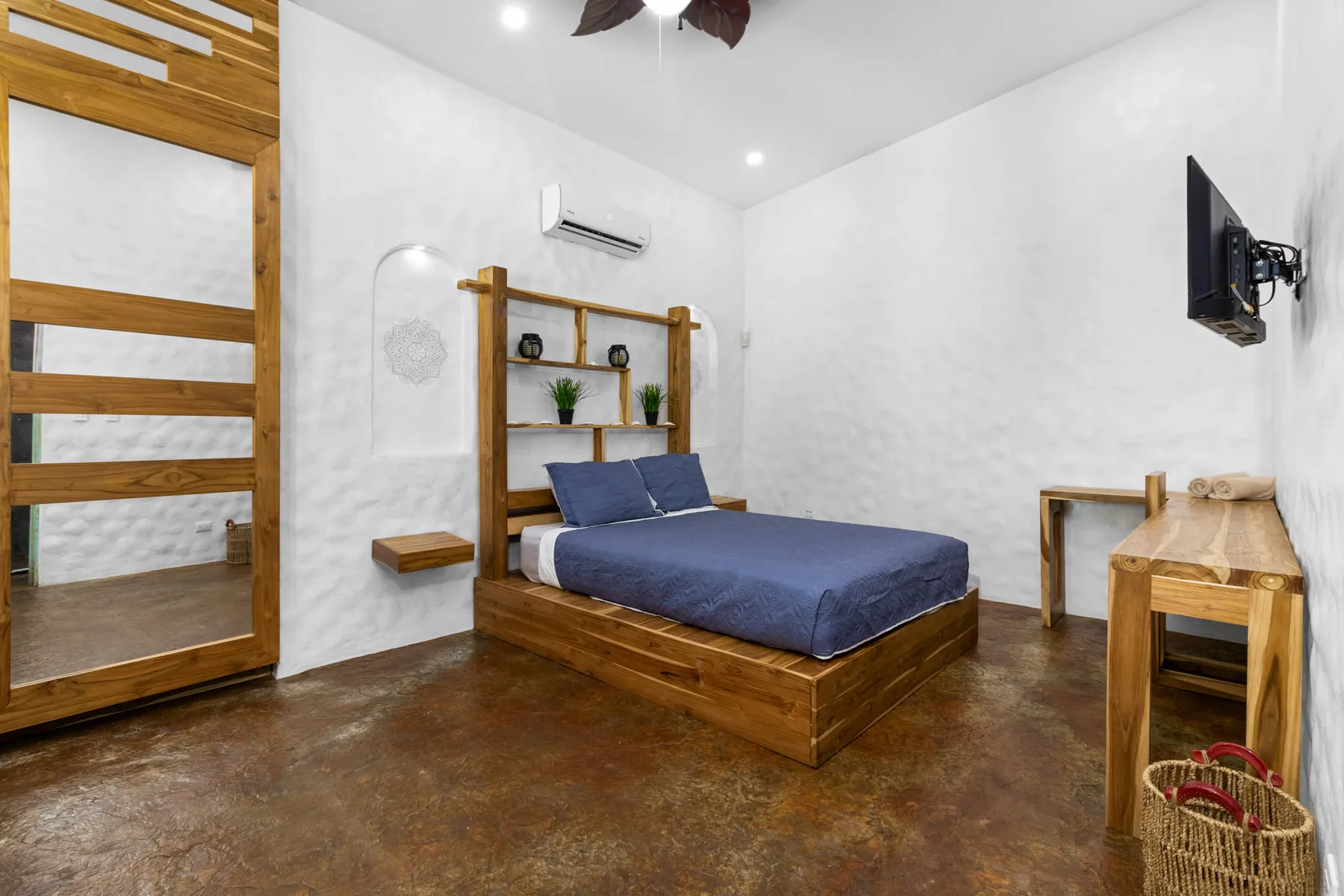 Un dormitorio con una cama de madera, ropa de cama azul y un televisor en la pared.