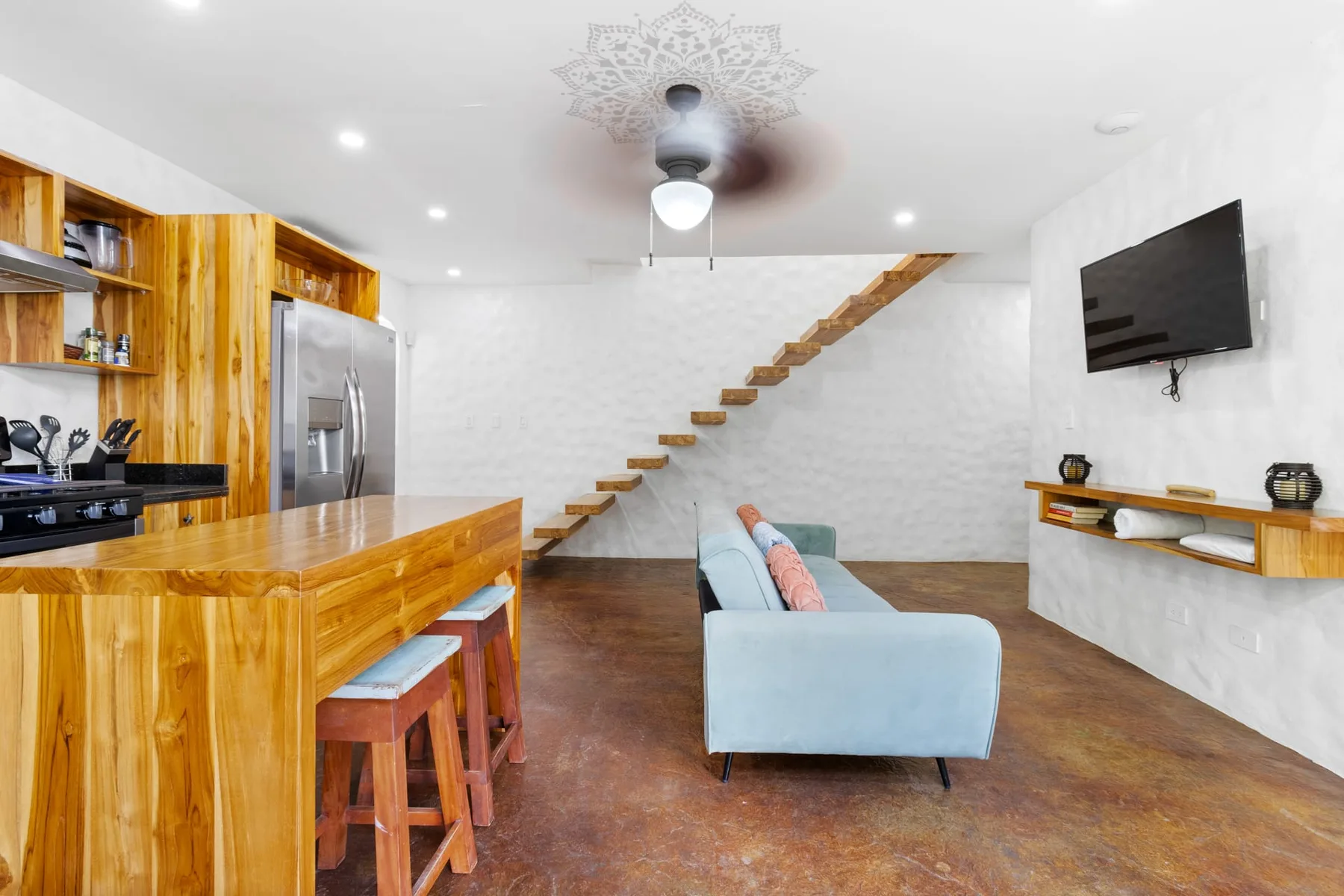 Sala de estar con un sofá azul claro, una barra de cocina de madera y una escalera abierta.