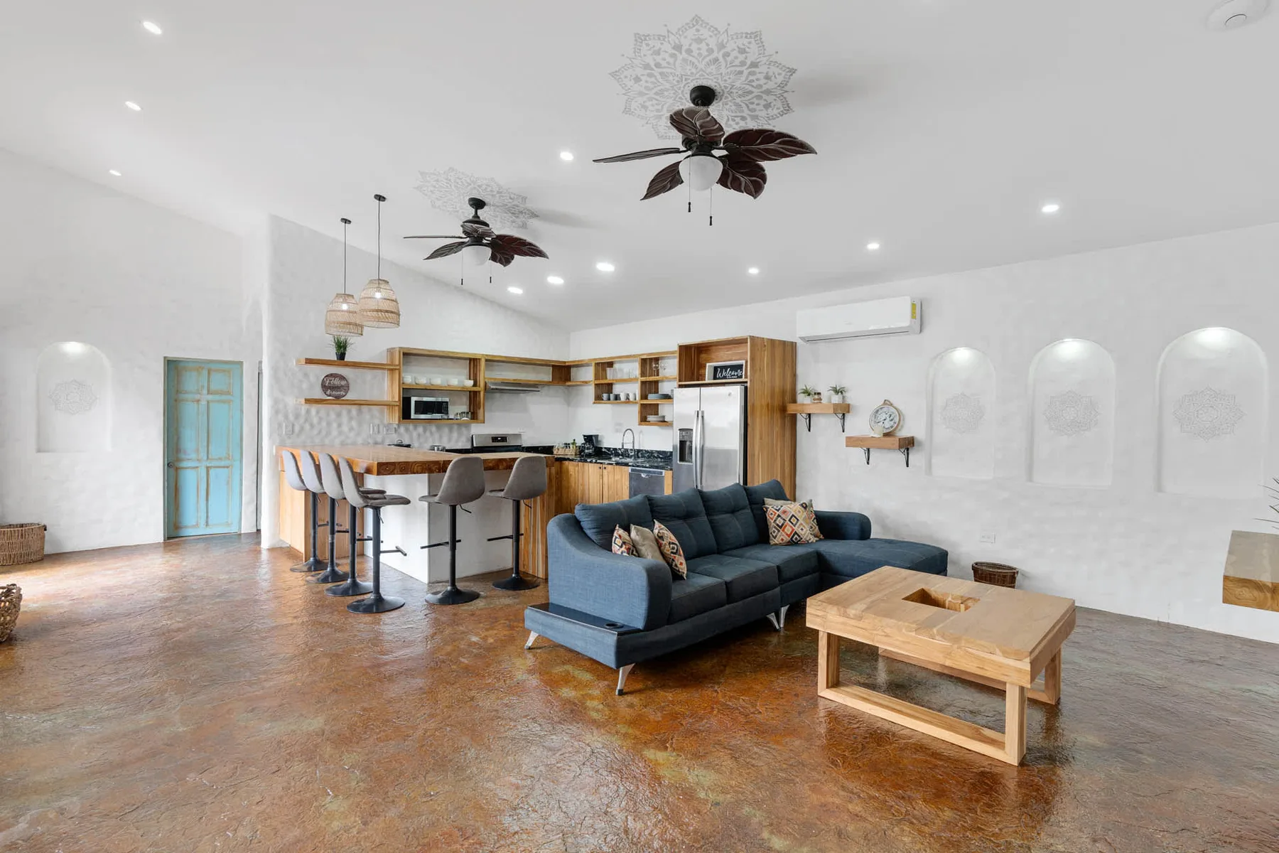 Sala de estar y cocina abiertas, con un sofá oscuro y una isla de madera.