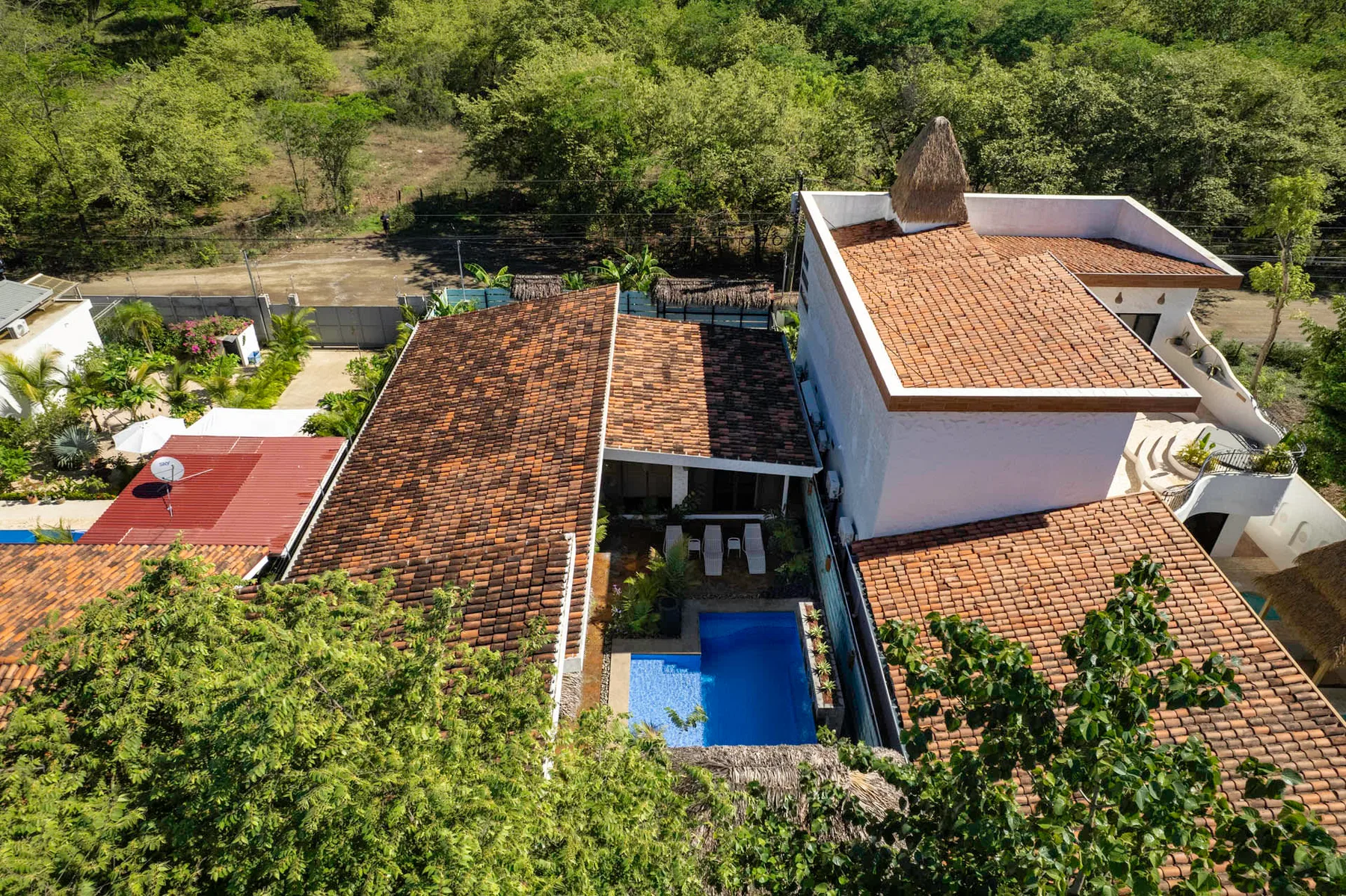 Vista aérea de una propiedad con tejados de tejas rojizas y una piscina azul entre árboles.