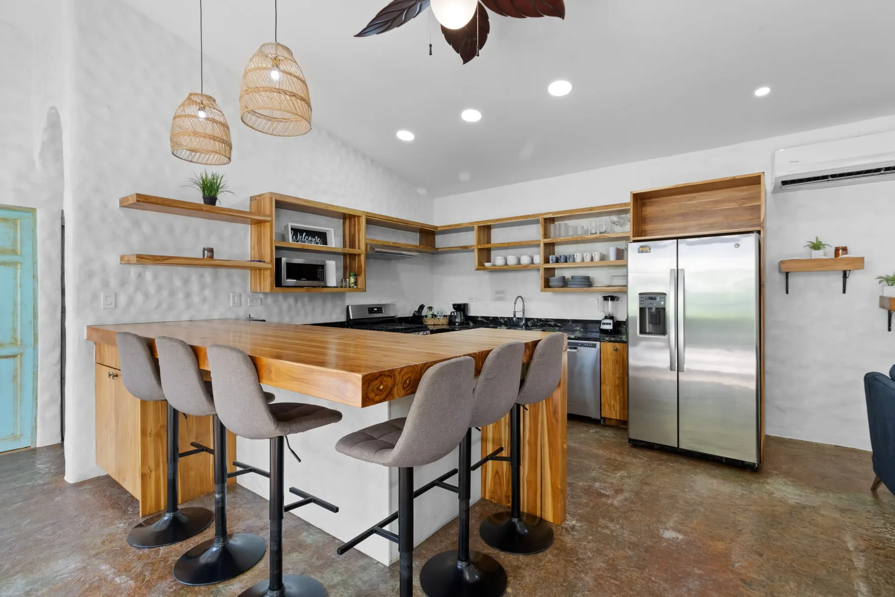 Una cocina con una larga isla de madera, asientos de barra y electrodomésticos de acero inoxidable.