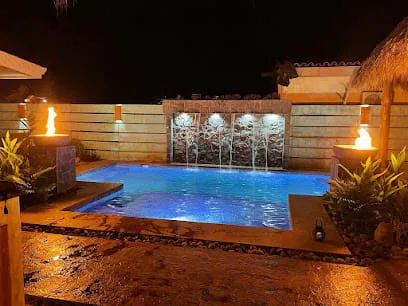 Una piscina exterior iluminada por la noche, junto a una cascada.