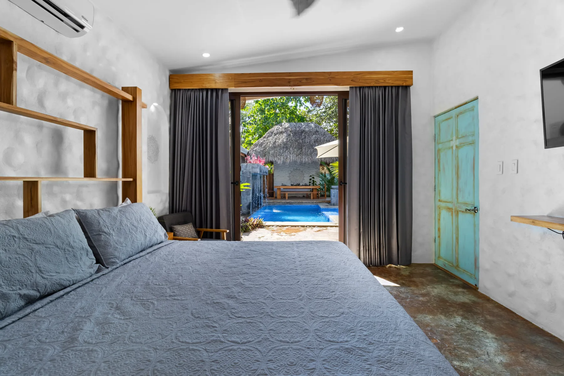 Un dormitorio con una cama grande frente a unas puertas abiertas hacia una zona de piscina.