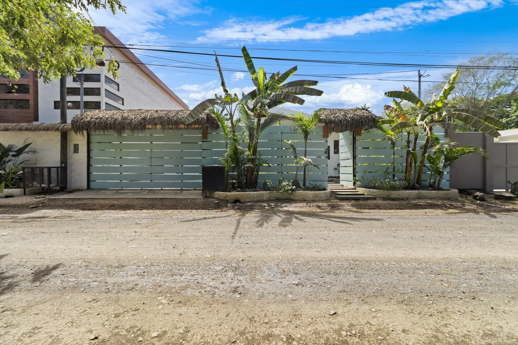 Una entrada cerrada da a un camino de grava, con plantas tropicales junto a la cerca.