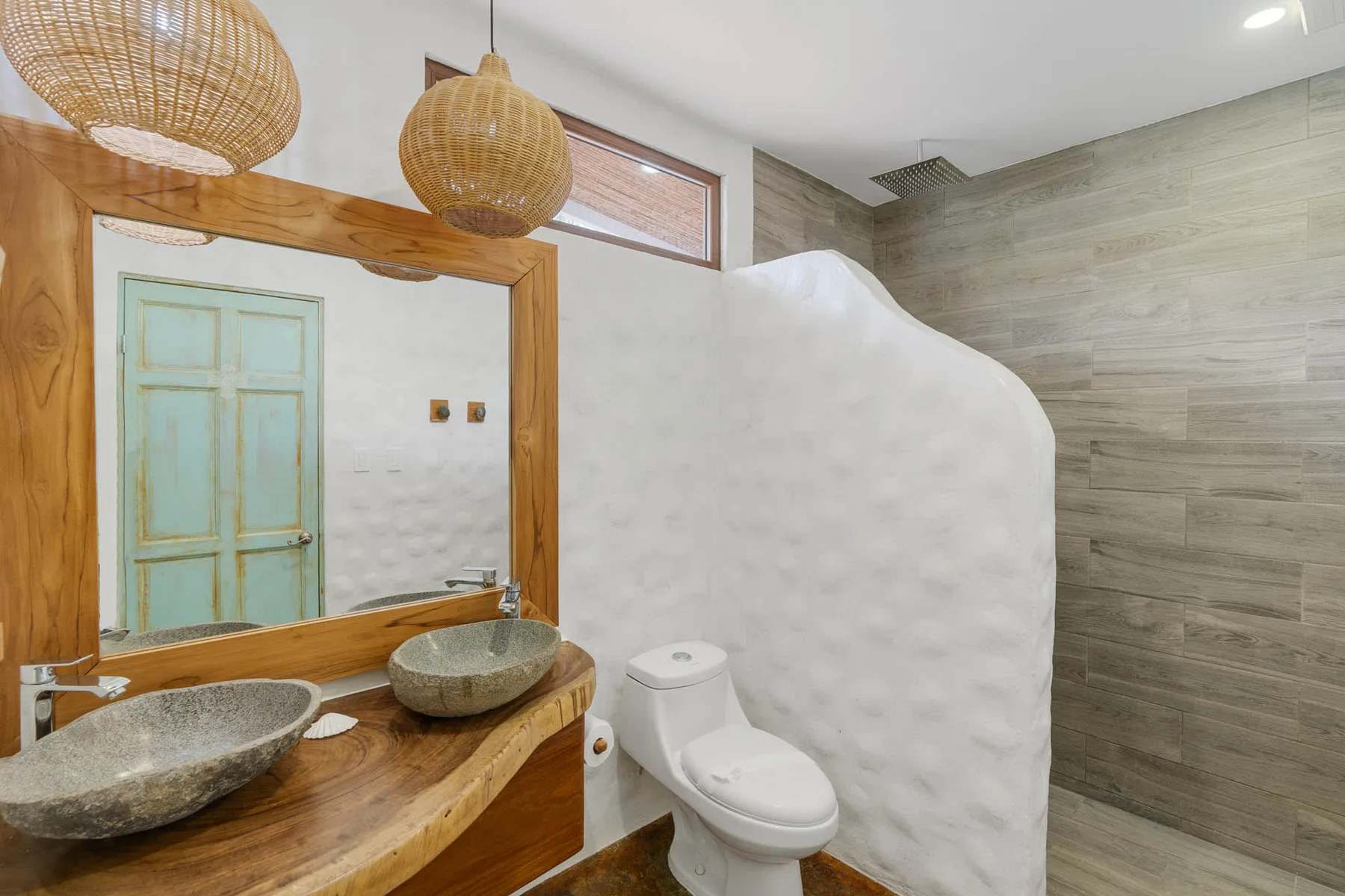 Un baño con lavabo de madera, lavabos sobre encimera y un inodoro detrás de un tabique curvo.