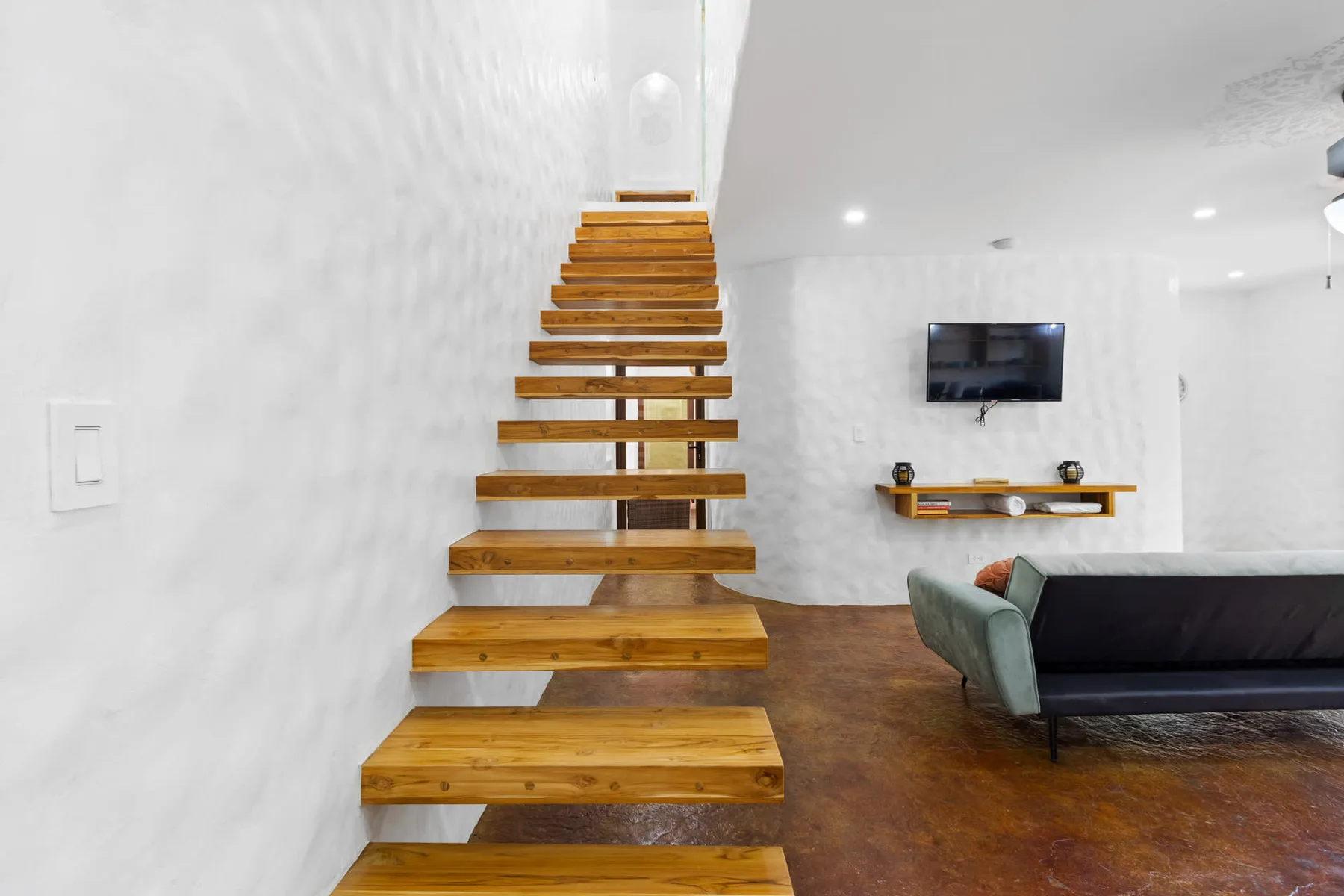 Una sala moderna con una escalera abierta de madera y un televisor montado en la pared.