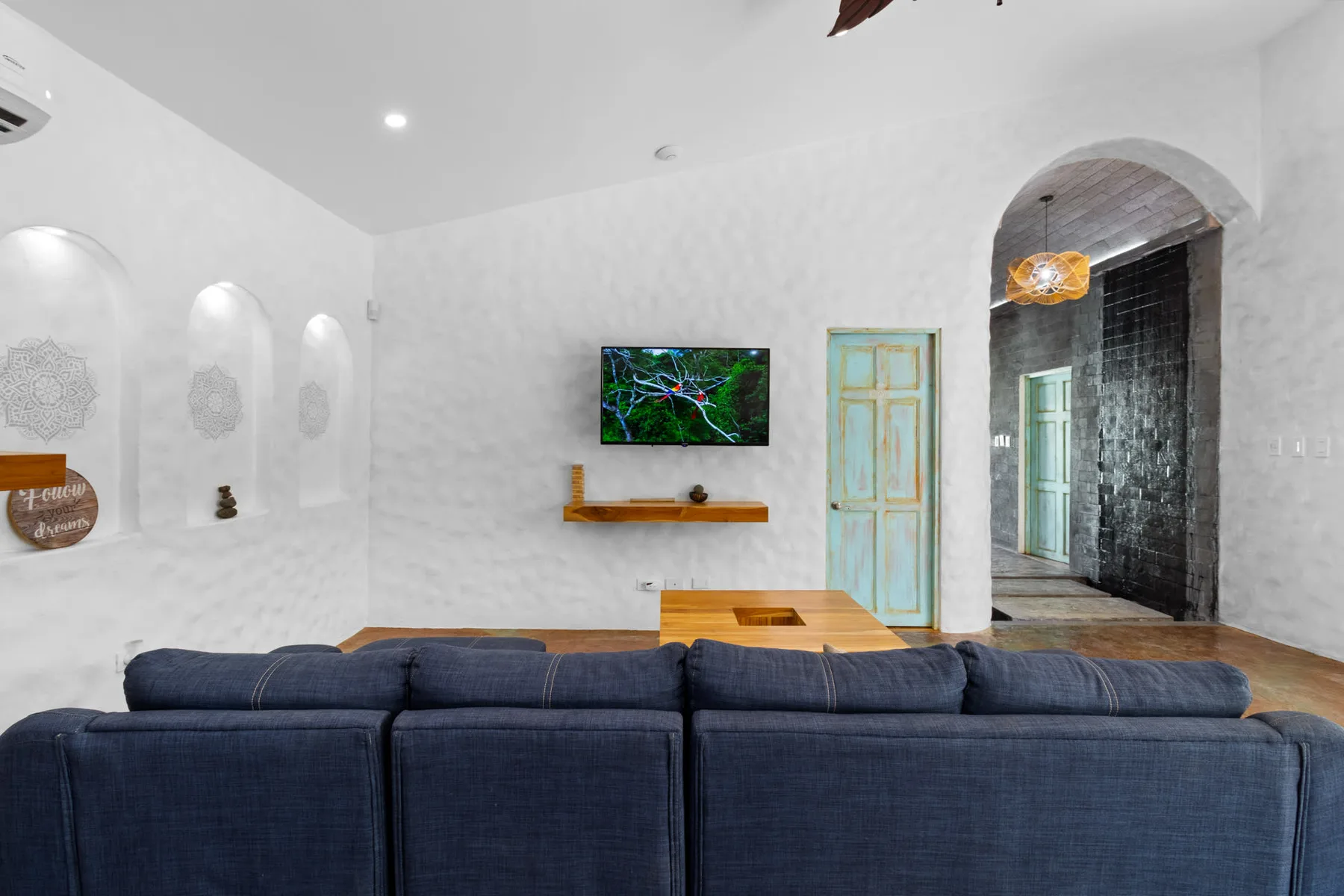 Una sala de estar con asientos oscuros, un televisor en la pared y una puerta arqueada.