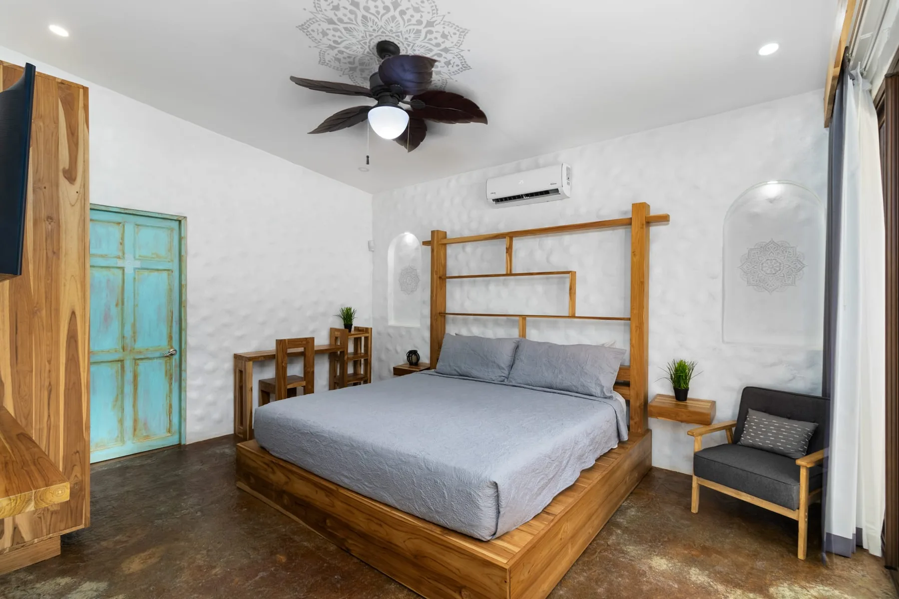 Un dormitorio con una cama de madera, ropa de cama gris y un pequeño escritorio junto a la puerta.