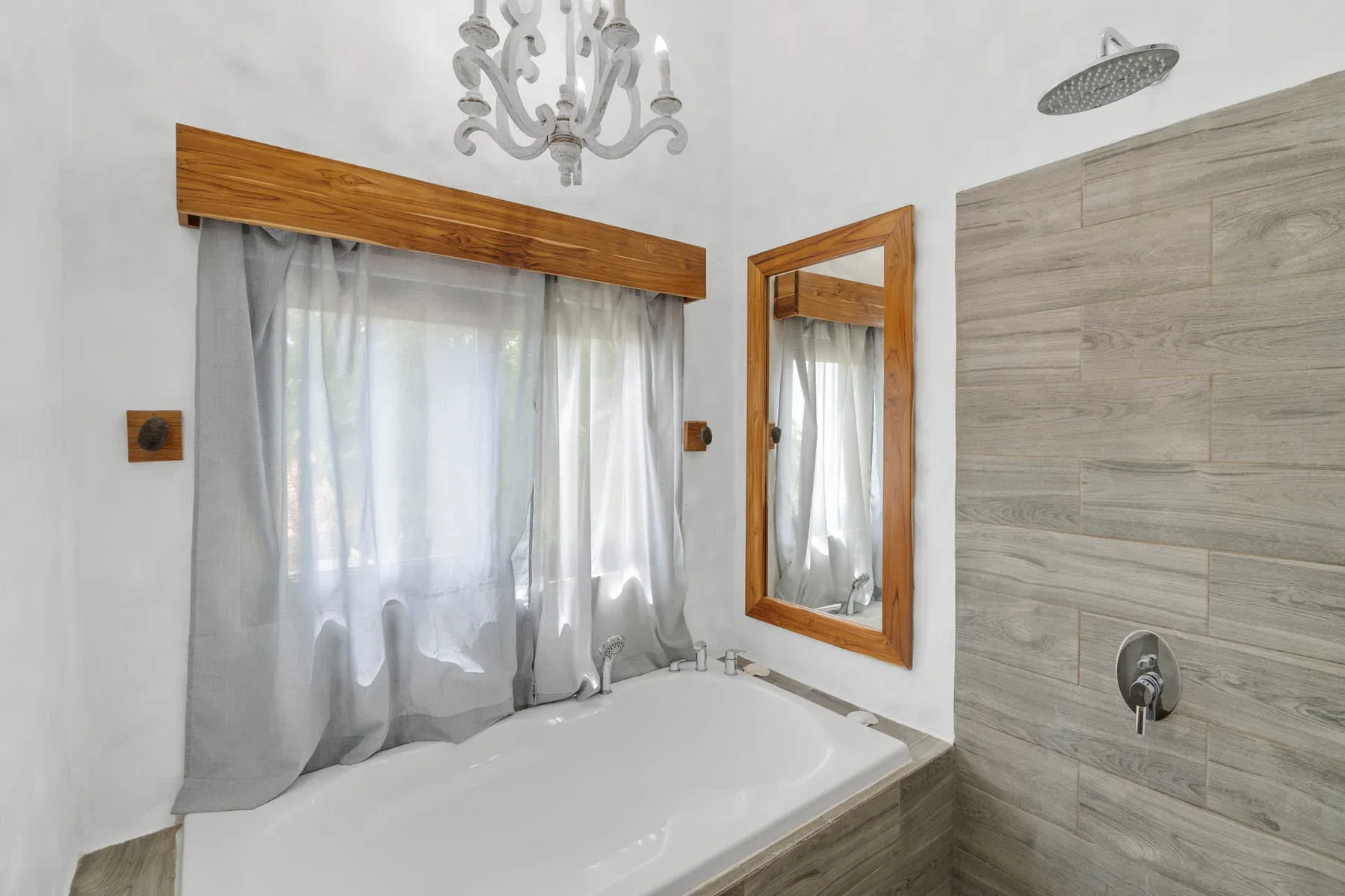 Un baño con bañera junto a una pared de ducha revestida y una ventana con cortinas.