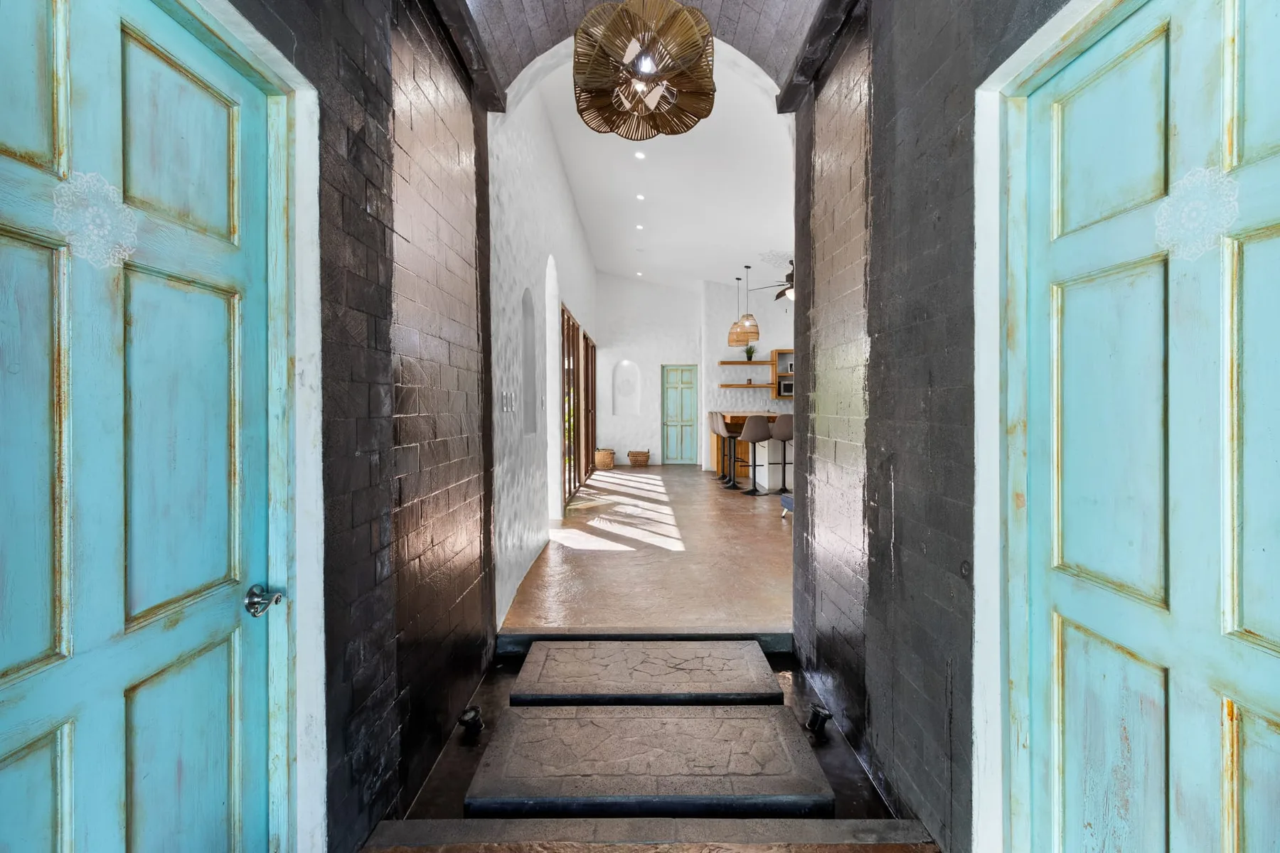 Un pasillo de entrada da a un interior luminoso con puertas turquesas y un comedor.