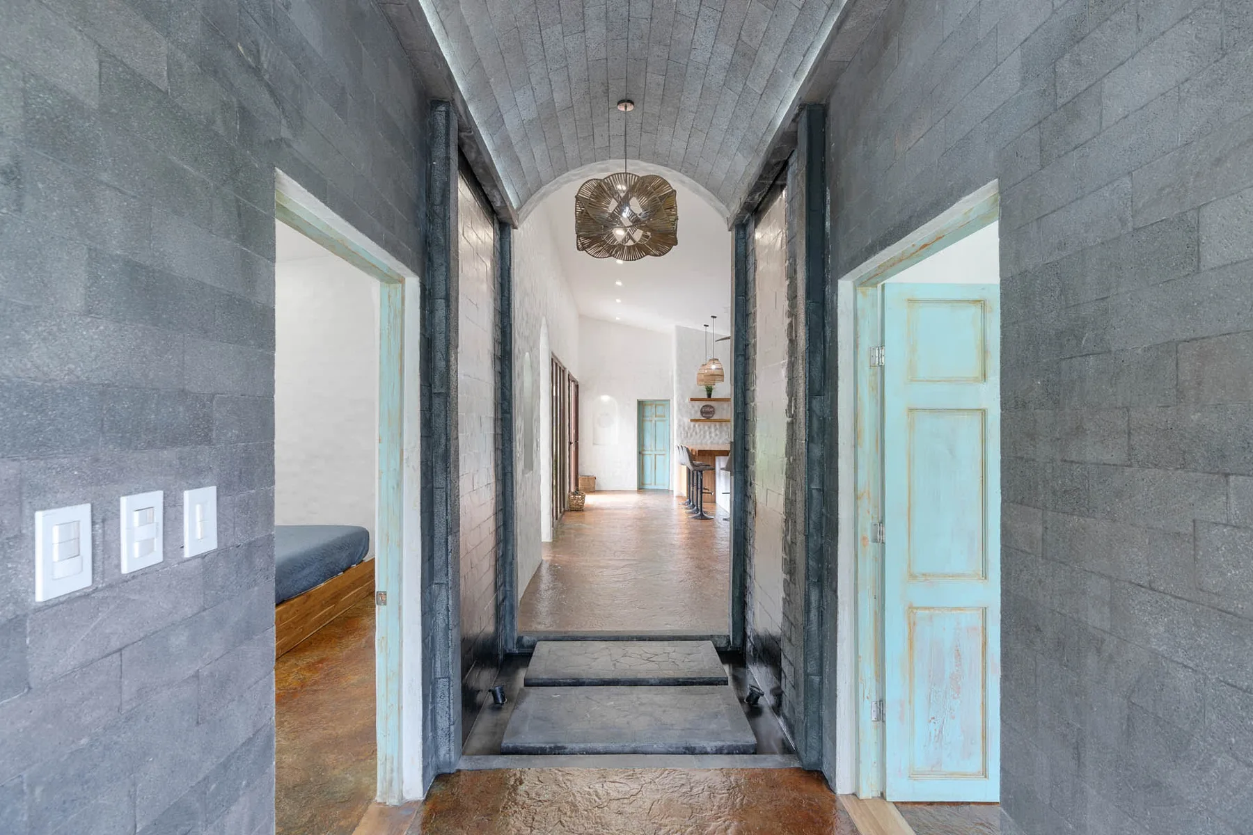 Un largo pasillo interior con paredes grises de piedra y puertas abiertas.