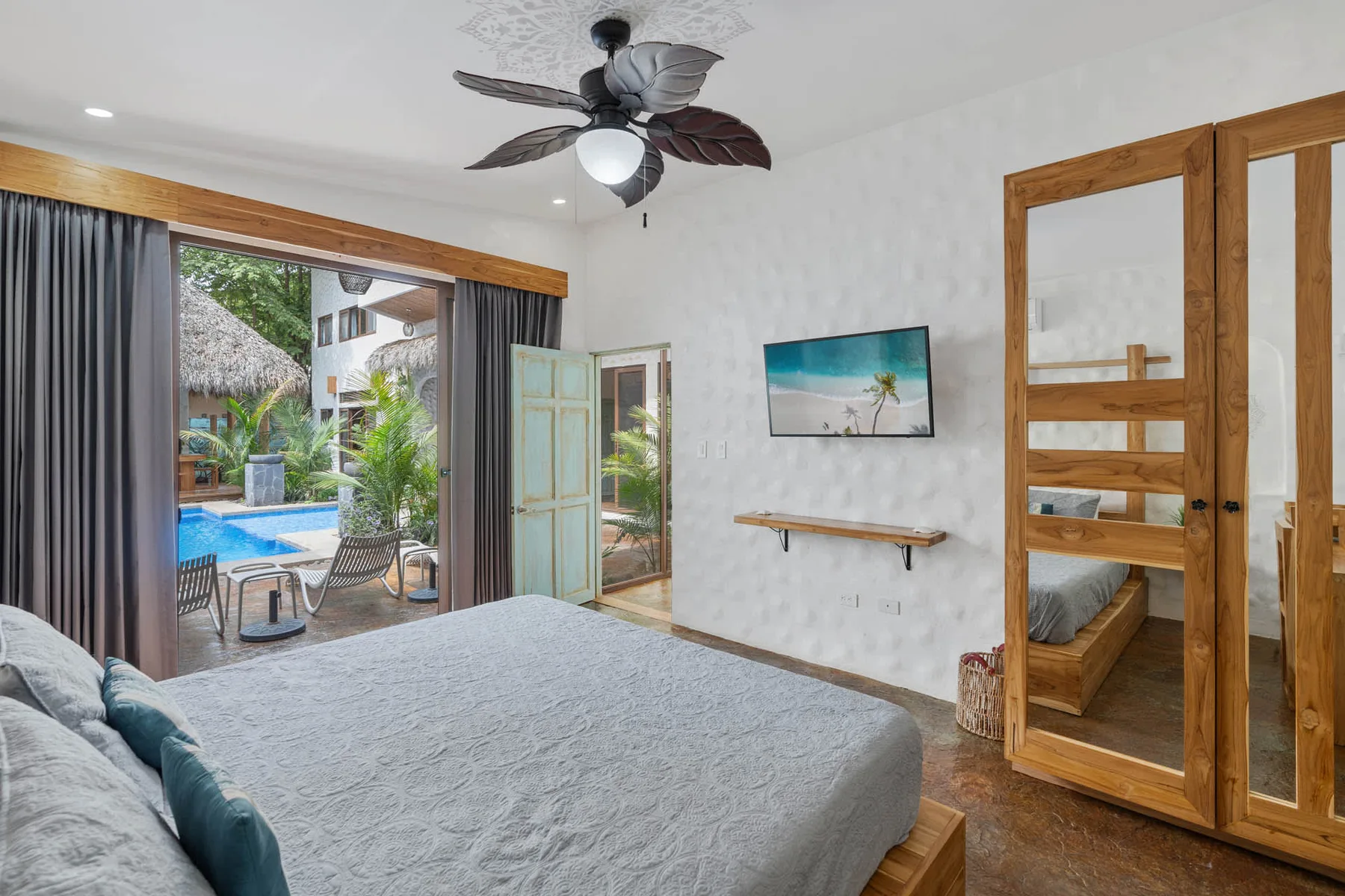 Un dormitorio con una cama grande, ventilador de techo y puertas abiertas hacia una zona con piscina.