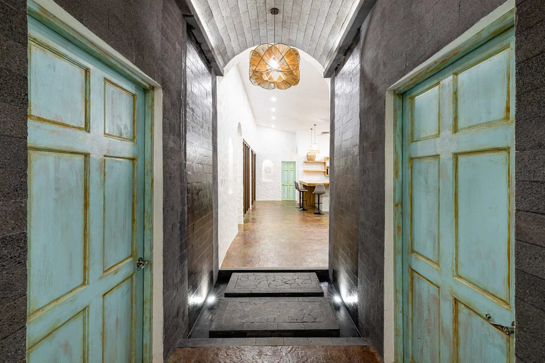 Un pasillo de entrada de piedra se abre a un interior luminoso con puertas turquesas.