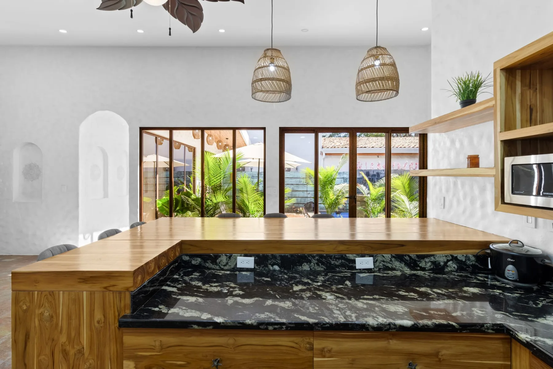 Una cocina moderna cuenta con una gran isla de madera, encimeras oscuras y ventanas con vista a la vegetación.