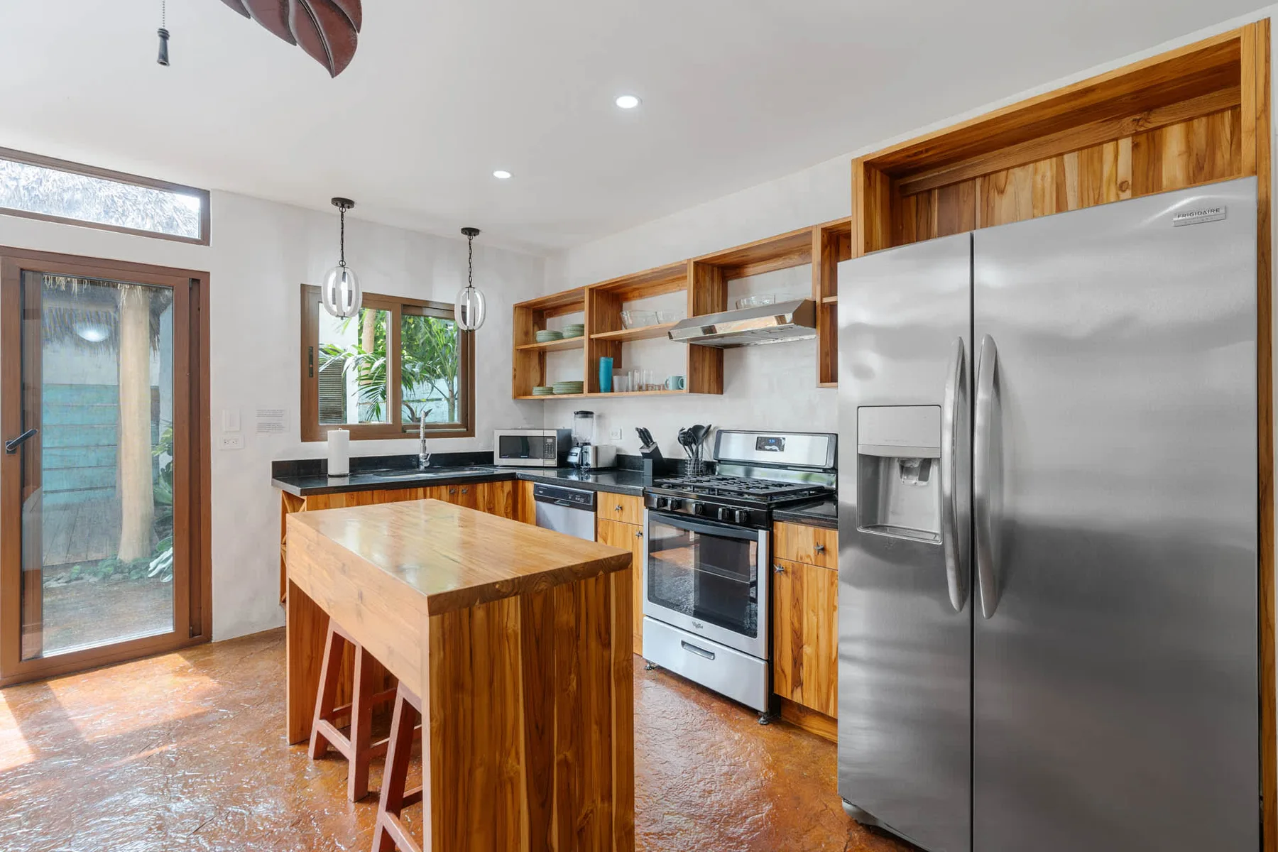 Una cocina luminosa con una isla de madera, electrodomésticos de acero inoxidable y estantes abiertos.