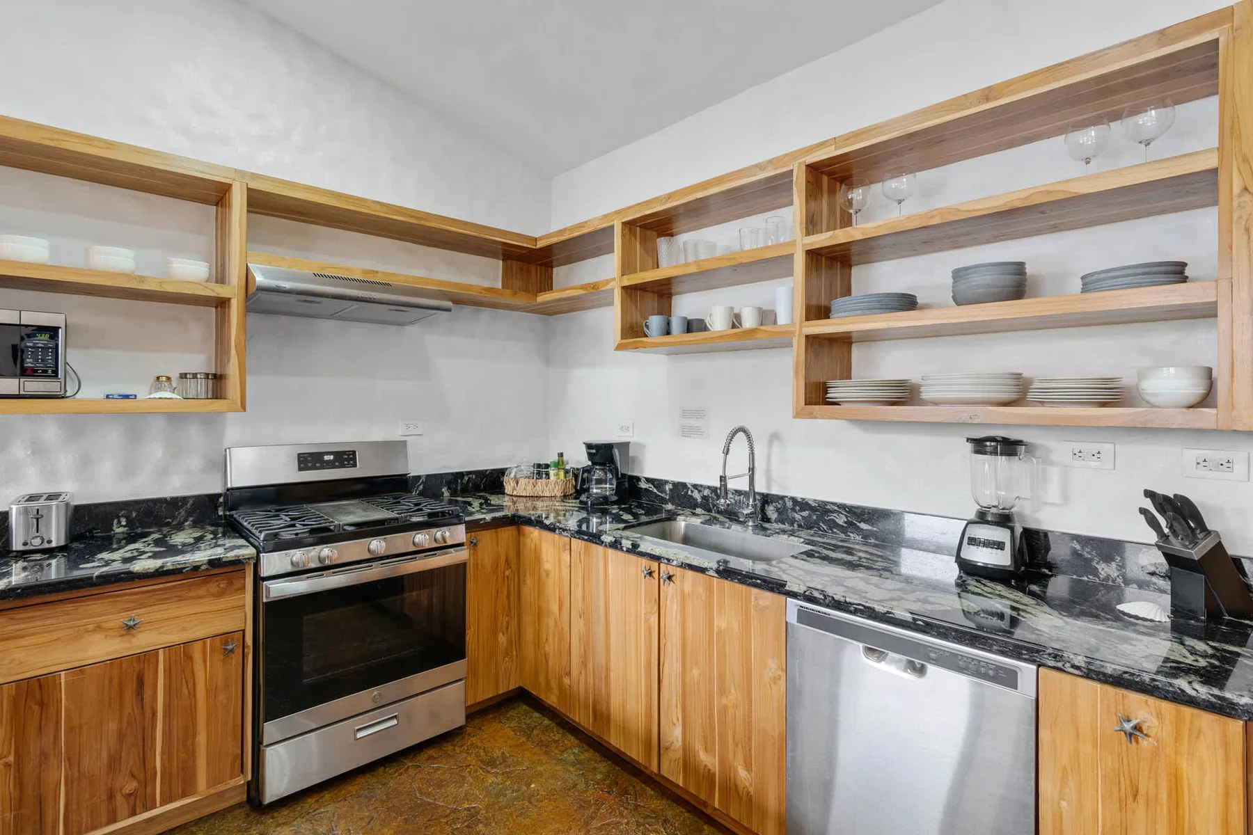Una cocina con gabinetes de madera, estantes abiertos y encimeras oscuras.