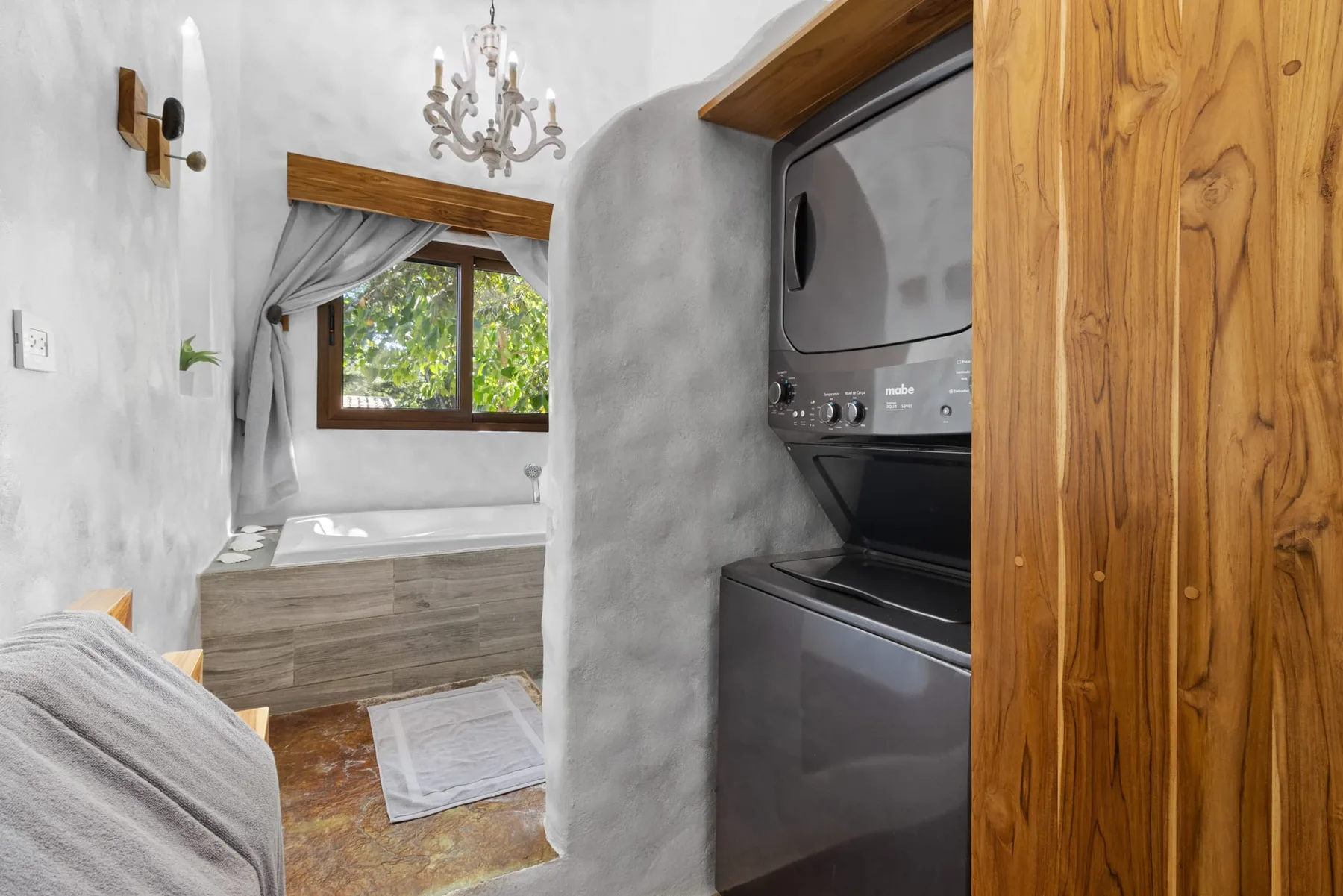 Un baño con bañera bajo una ventana y una lavadora-secadora al lado.