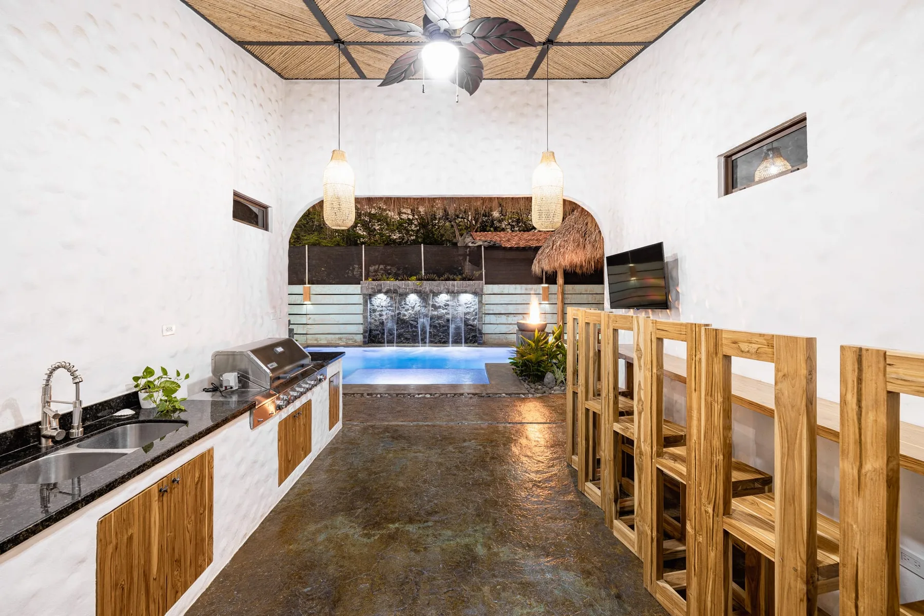 Una cocina y comedor interior se abren a una piscina con una pequeña cascada.
