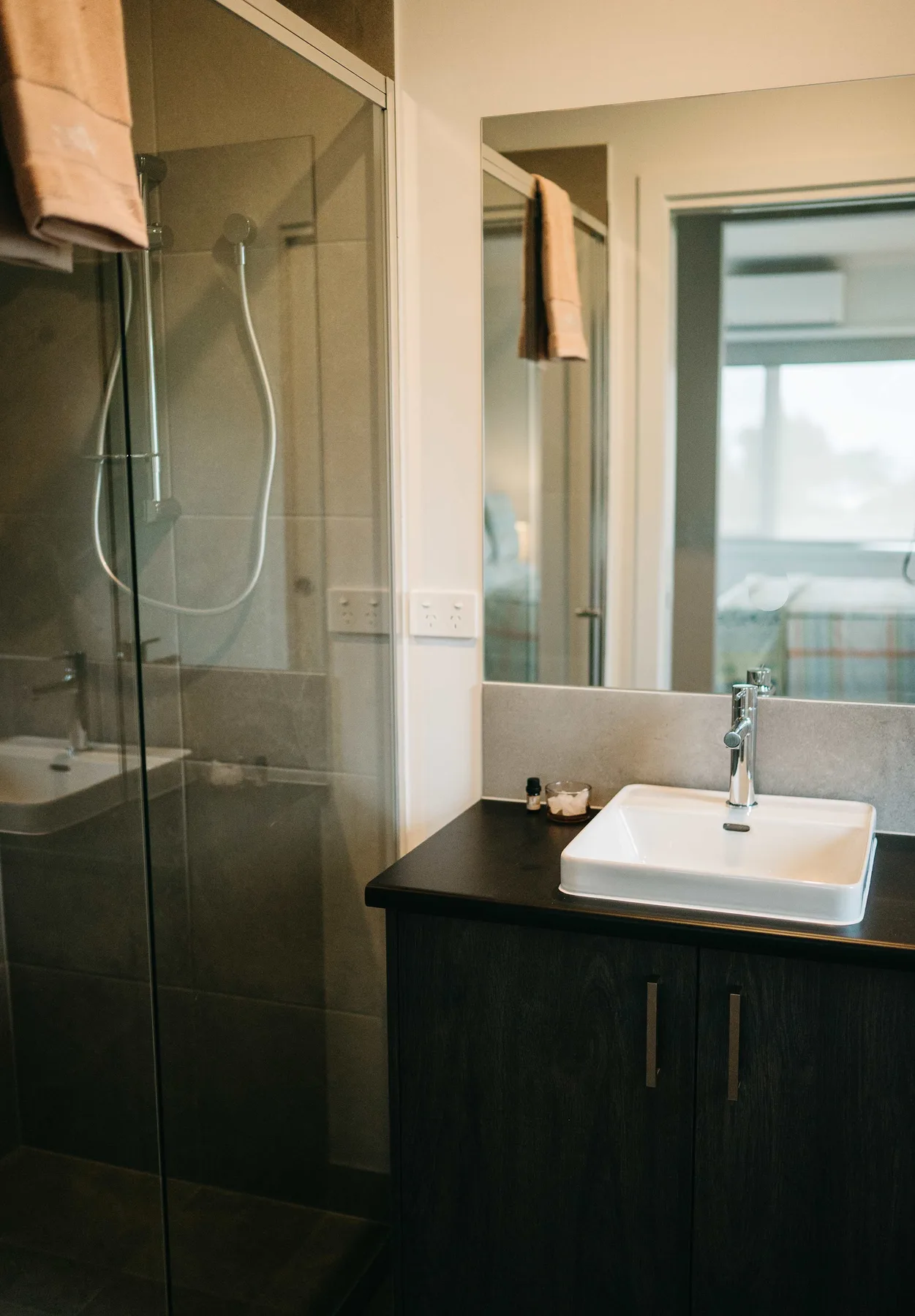 Un baño con una ducha de vidrio y un lavabo sobre un mueble oscuro.
