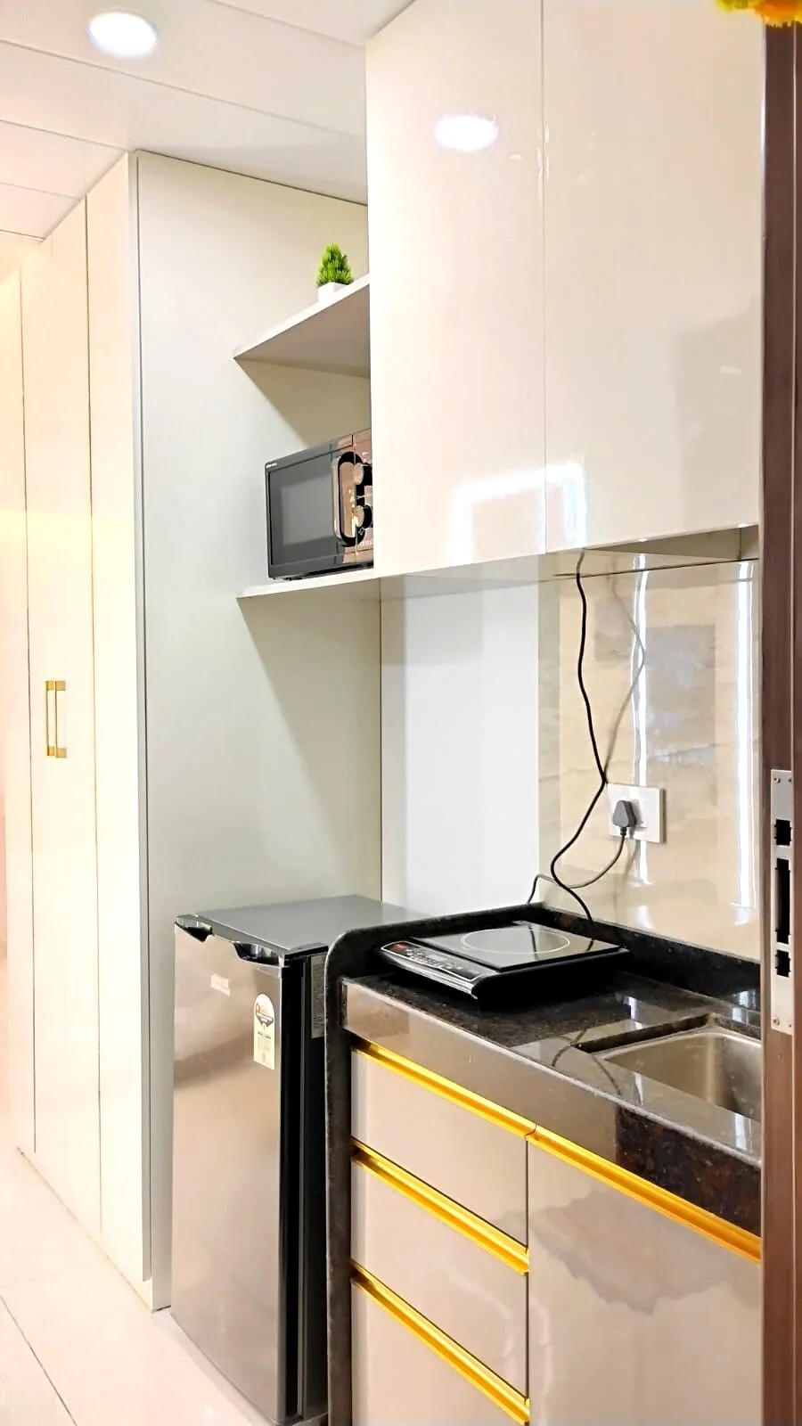 A compact kitchenette with a microwave, sink, and glossy cabinets.