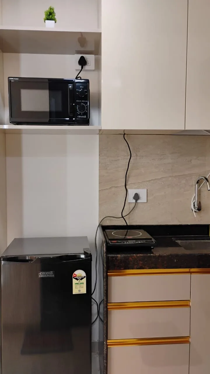 A compact kitchen area with a microwave, refrigerator, and dark countertop.