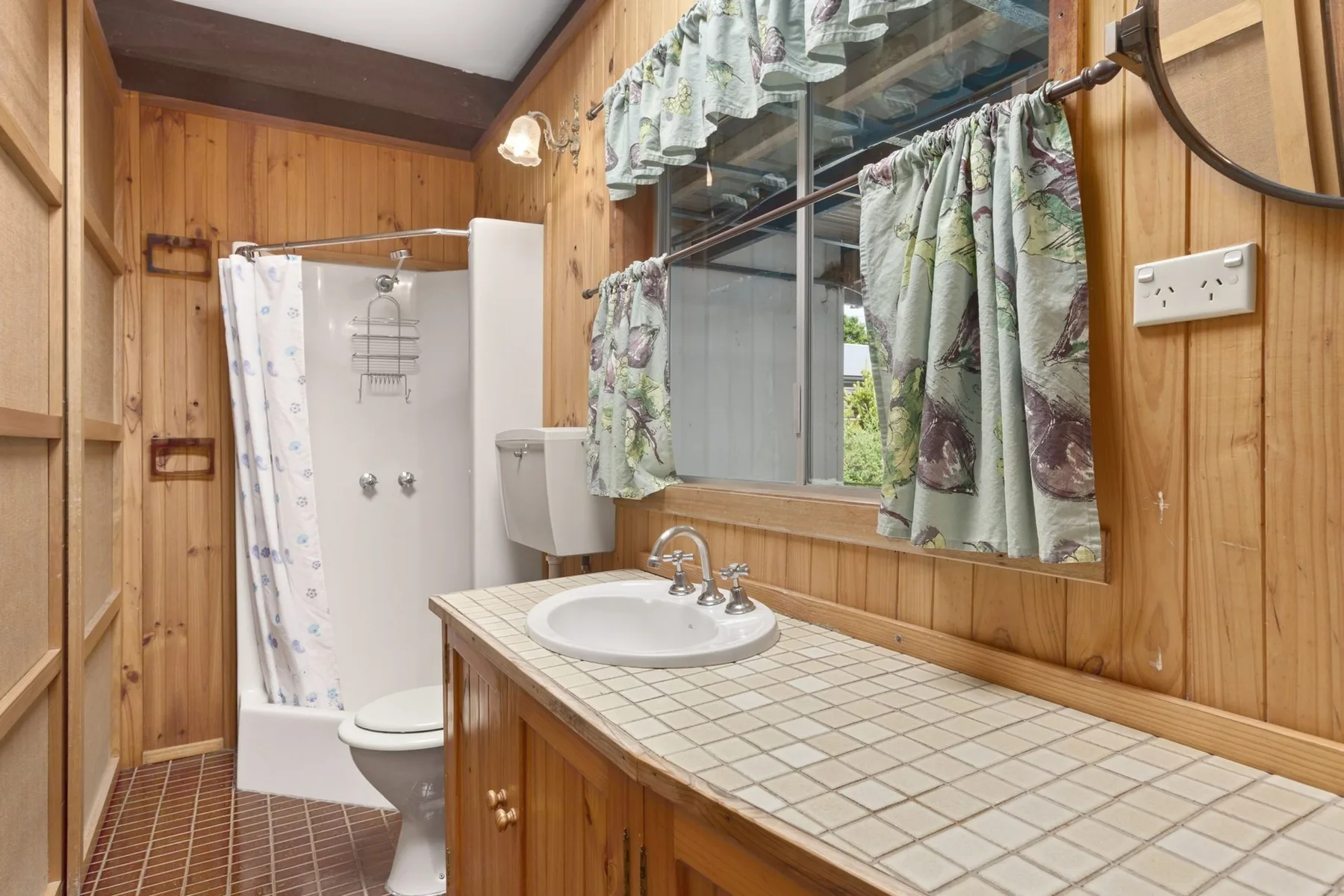 Un baño revestido de madera con un tocador de azulejos y una ducha con cortina.