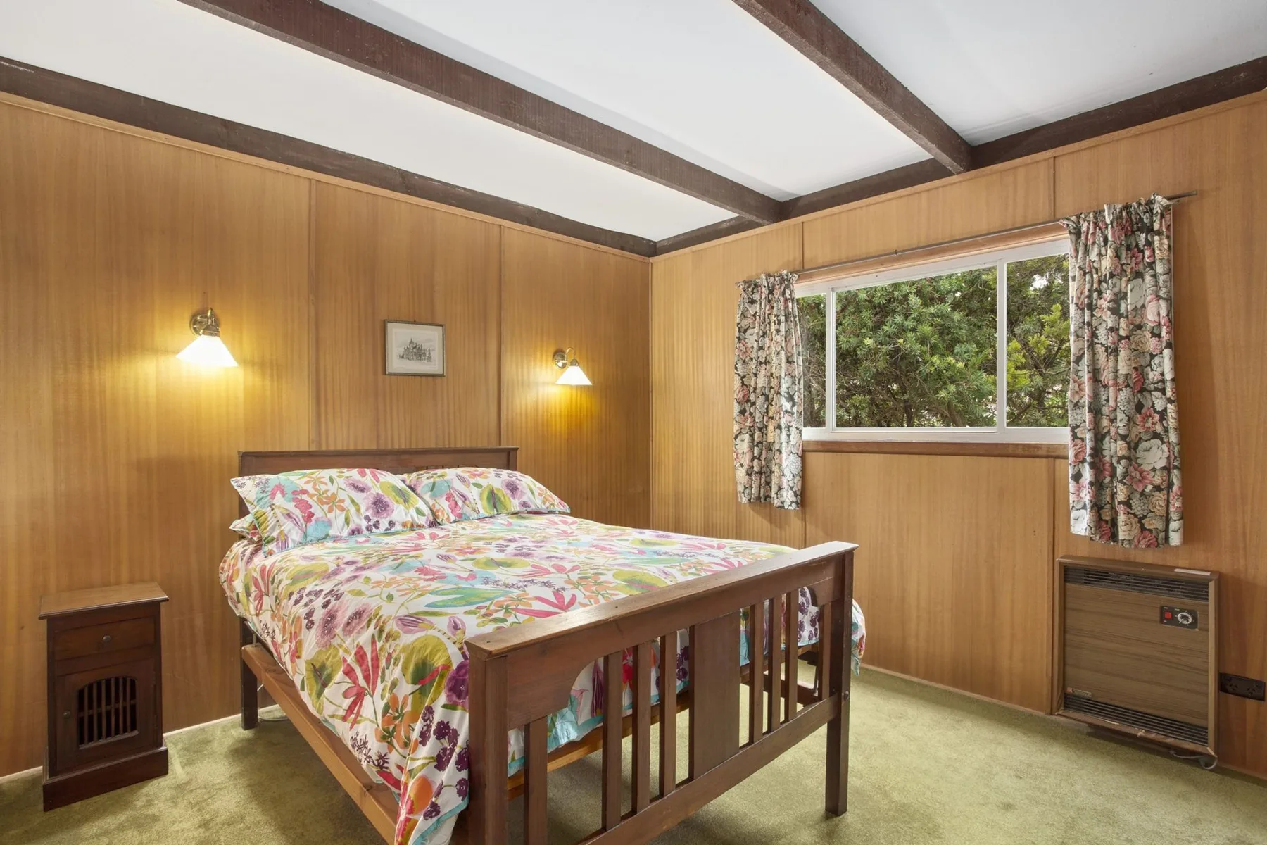 Un dormitorio con ropa de cama floral y una ventana con vistas a la vegetación.