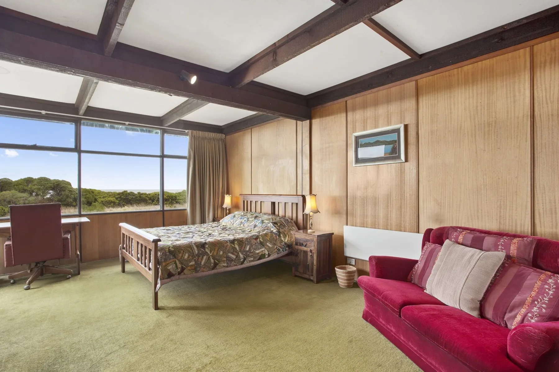Un dormitorio con una cama, un escritorio junto a las ventanas y un sofá rojo.