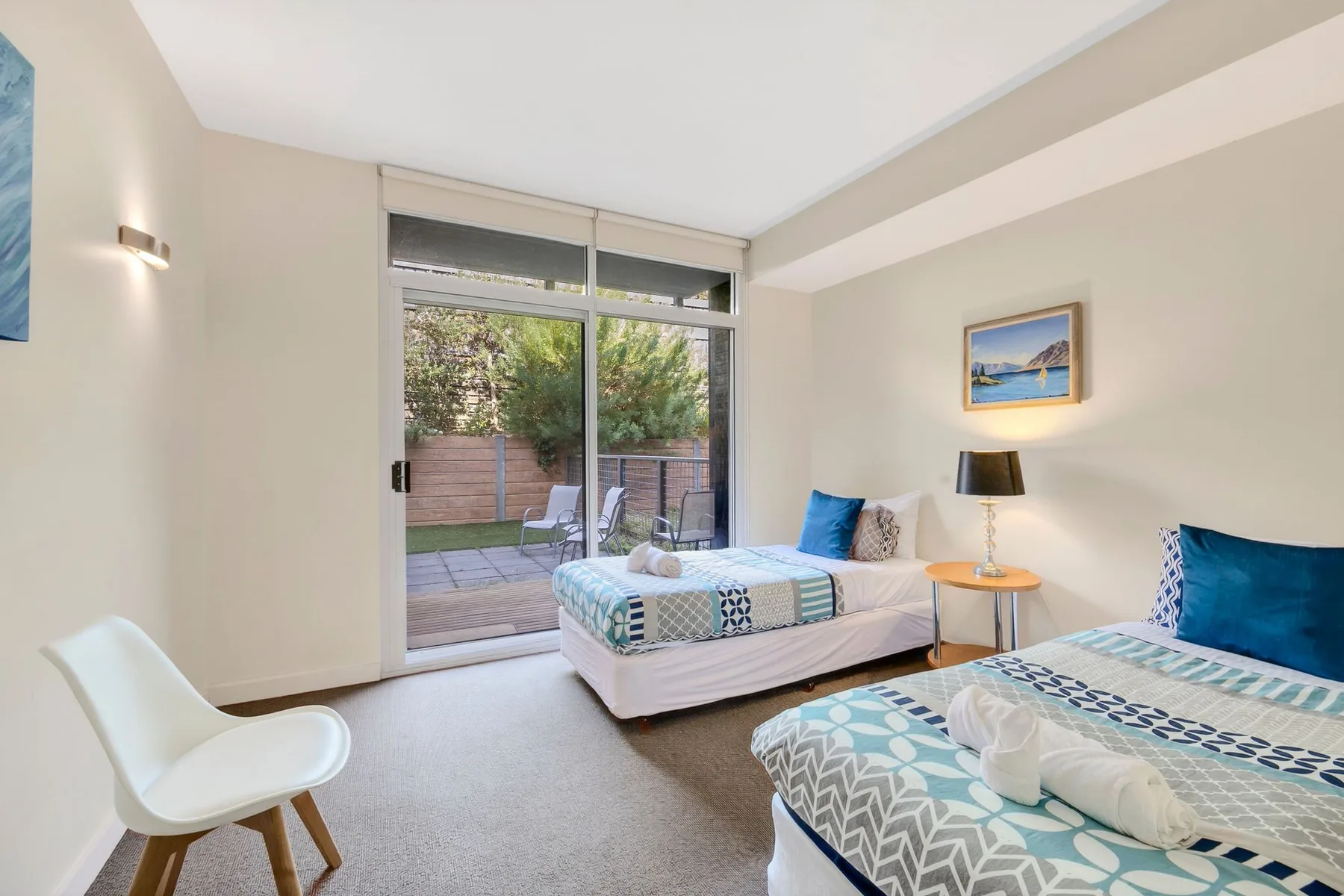 Un dormitorio luminoso con dos camas y una puerta corrediza de vidrio que da a un patio.