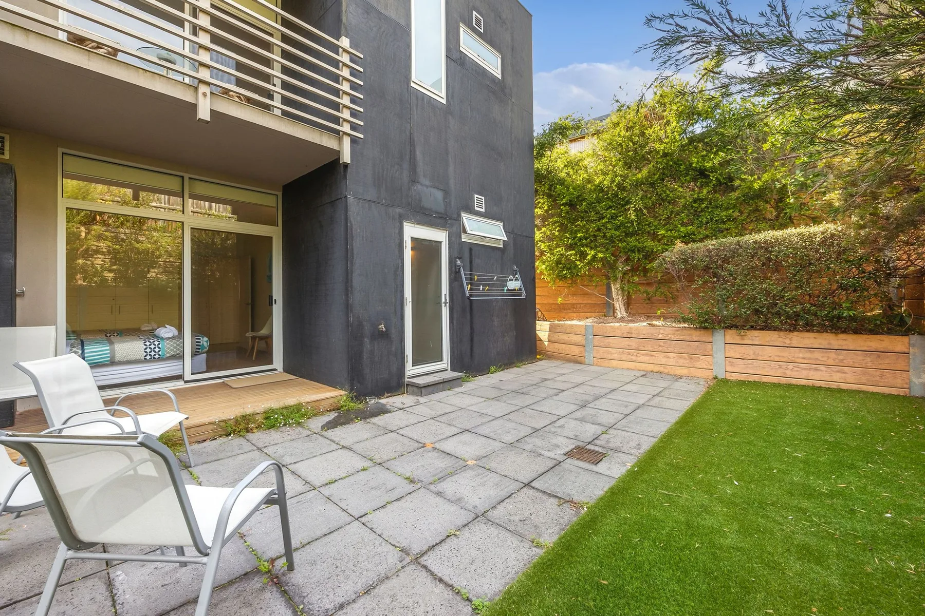 Un patio pavimentado junto a un edificio moderno, con asientos al aire libre y césped.