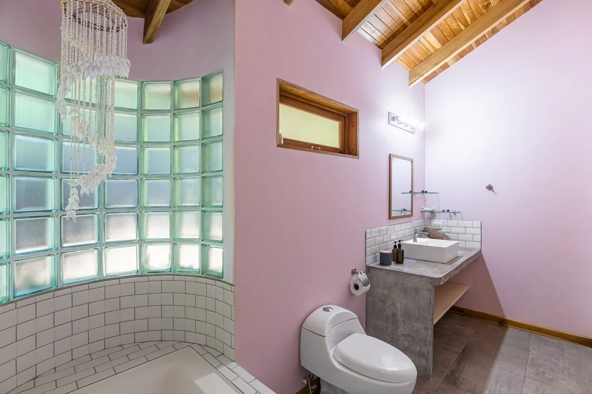 Un baño con ducha de bloques de vidrio, lavabo e inodoro bajo un techo de madera.