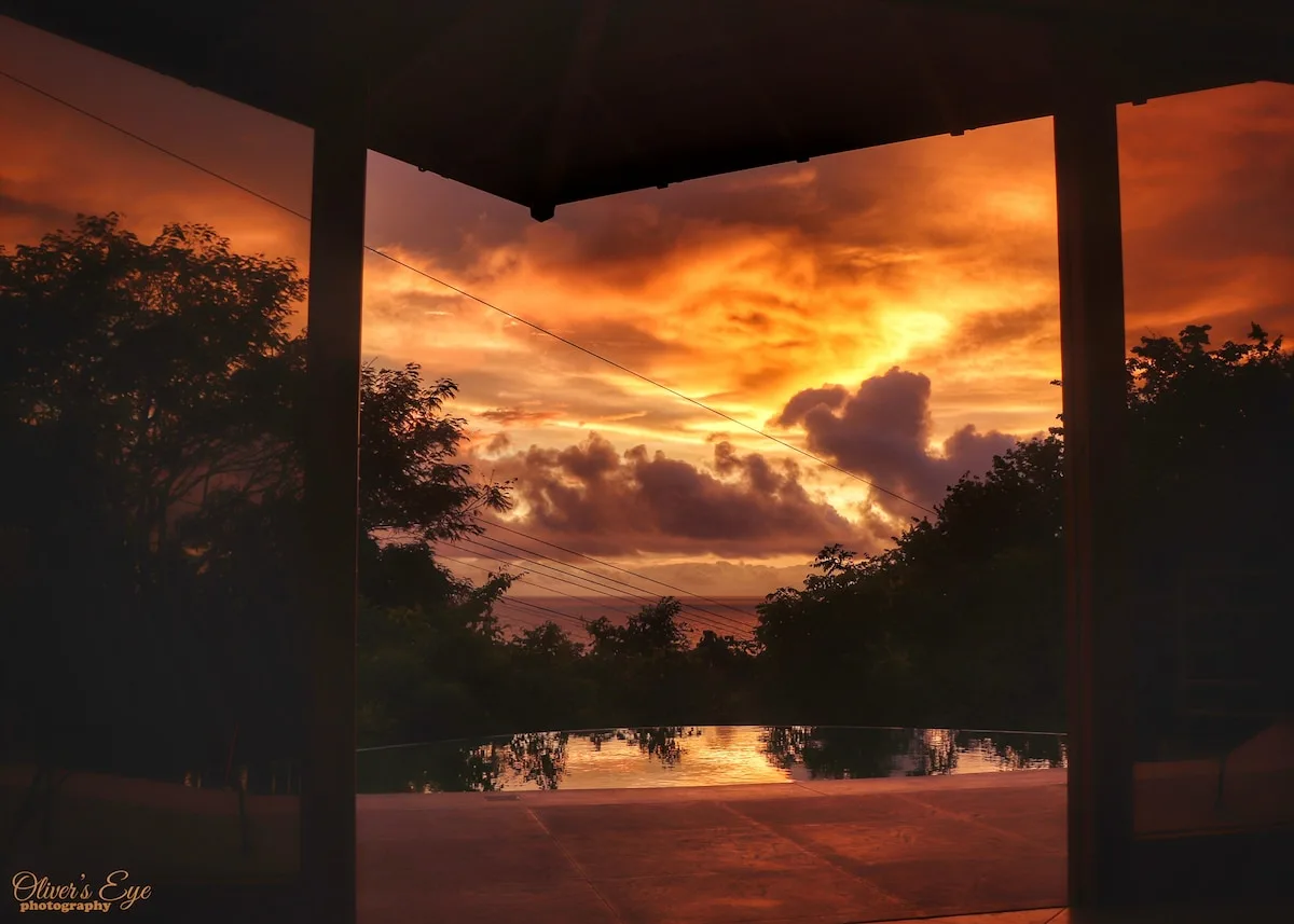 Un atardecer intenso brilla sobre árboles en silueta, visto desde un patio cubierto.
